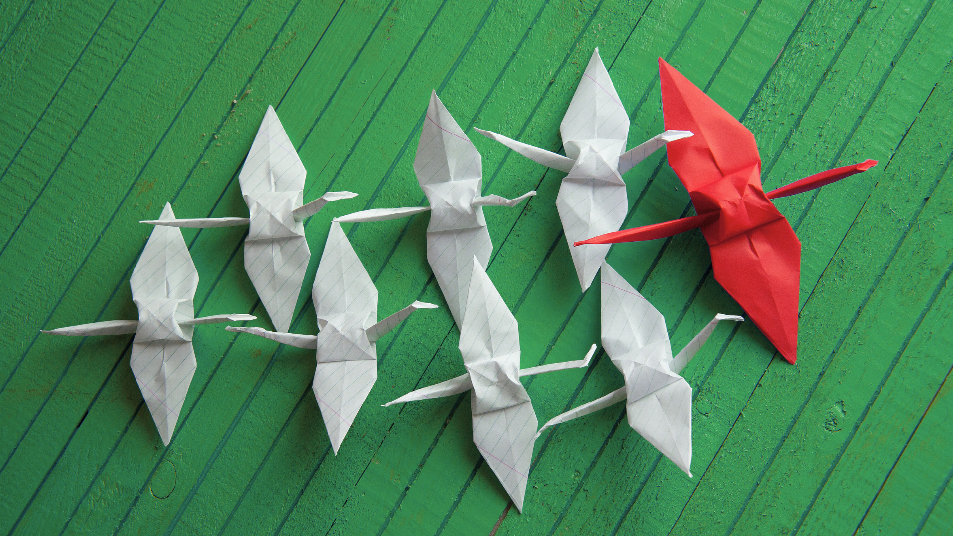 Origami birds with one red bird flying ahead of the group