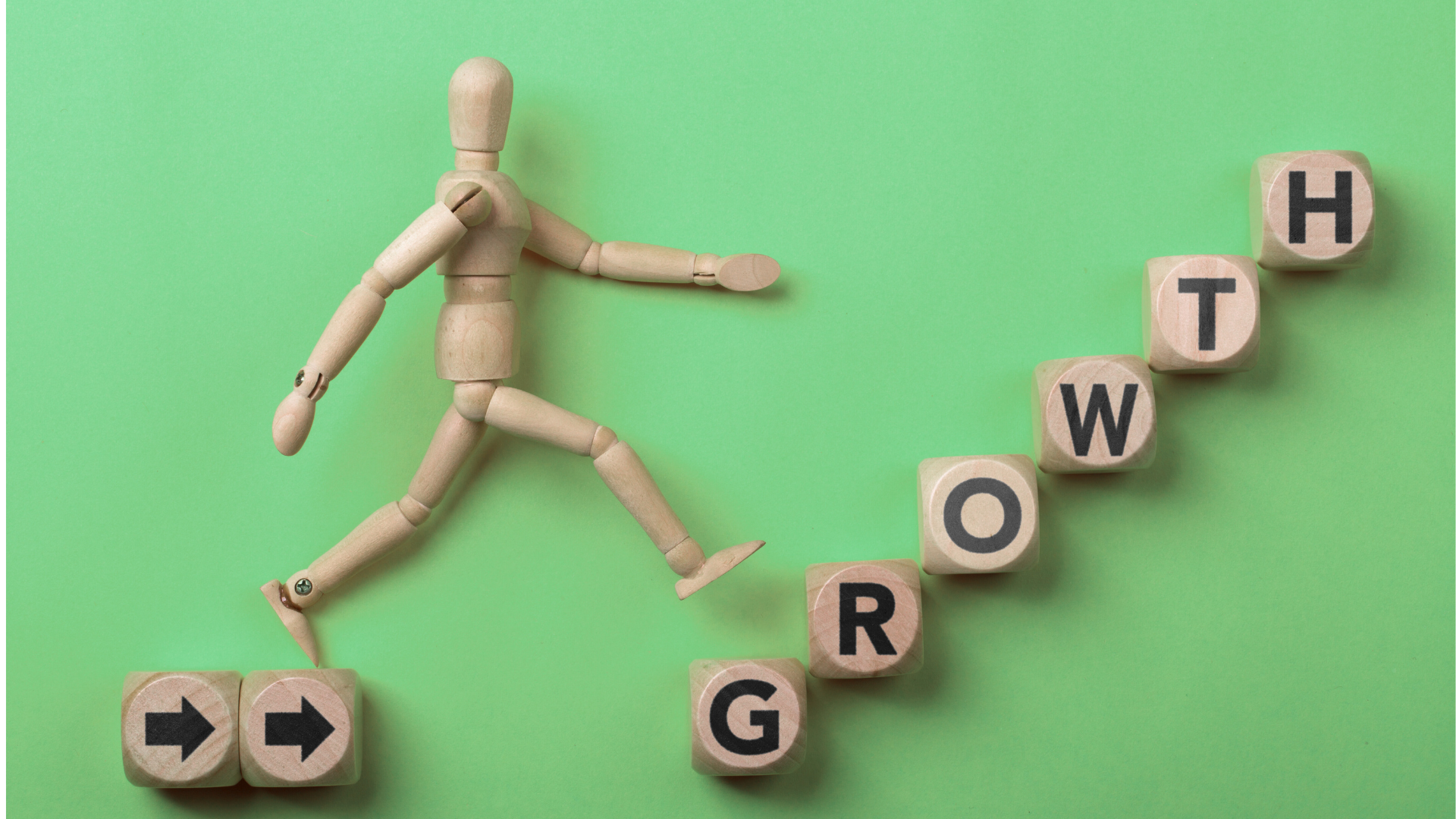 Wooden mannequin stepping upward on blocks spelling ‘GROWTH’