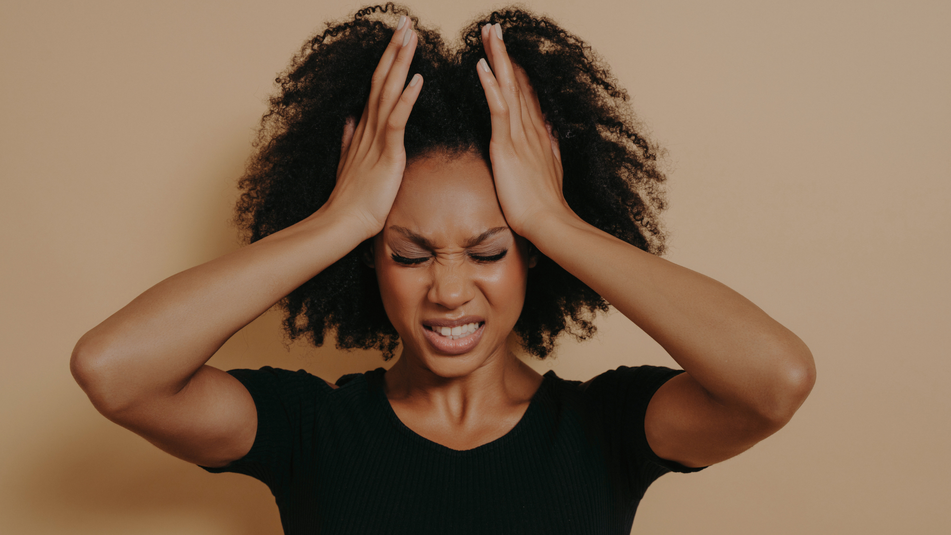 A woman presses her hands against the sides of her head, teeth clenched.