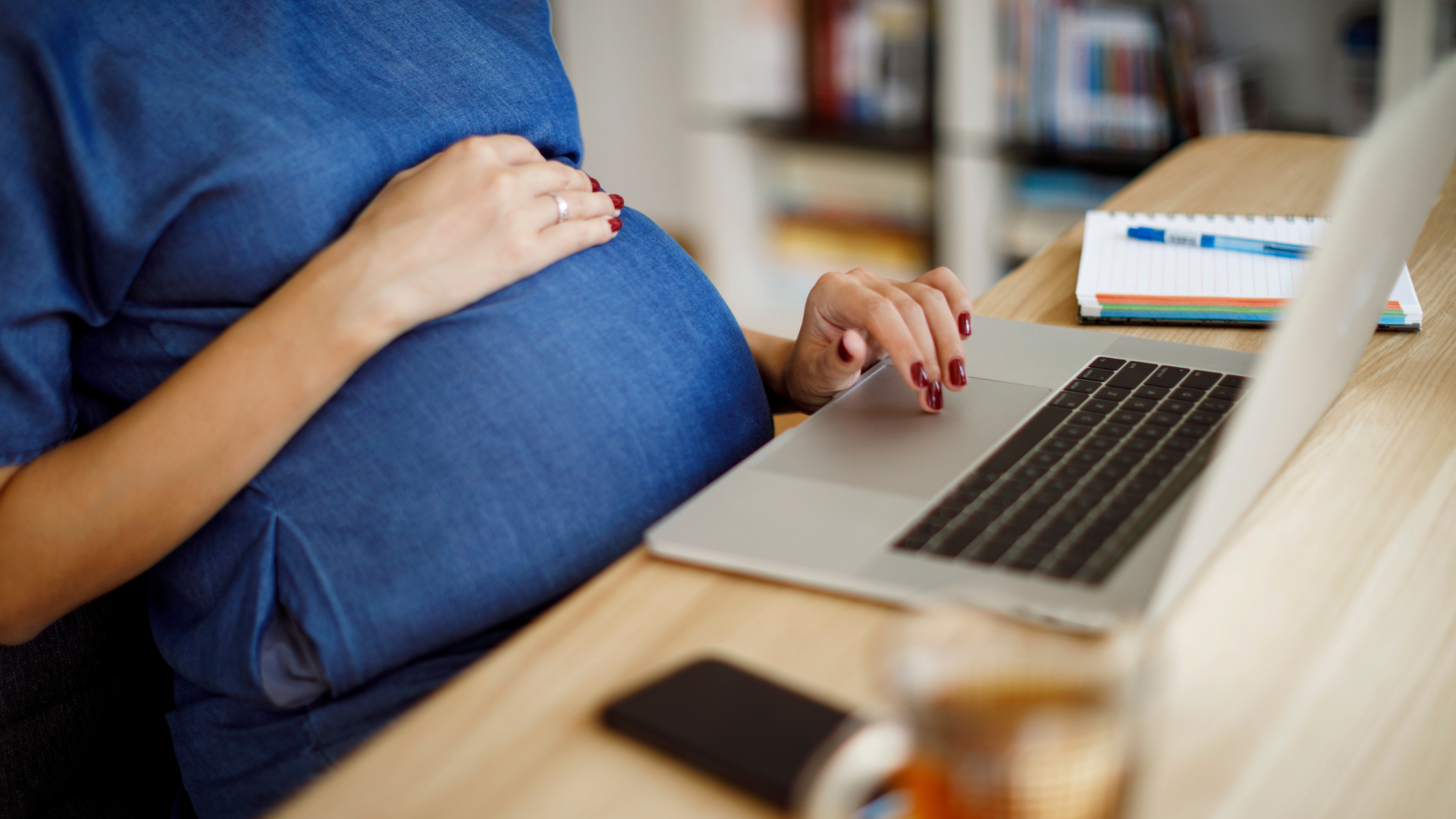 Pregnant woman typing on a laptop at a desk.