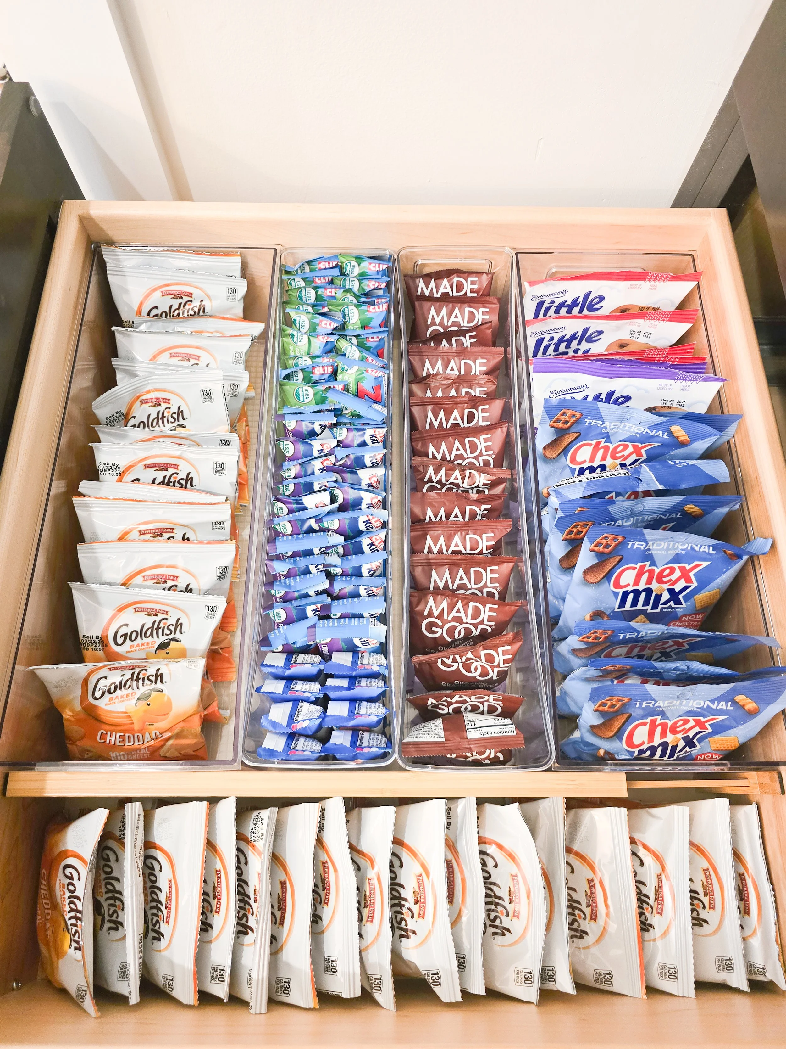 Organized snack drawer with clear acrylic bins holding individually packaged snacks for easy grab-and-go lunches and after-school snacks.
