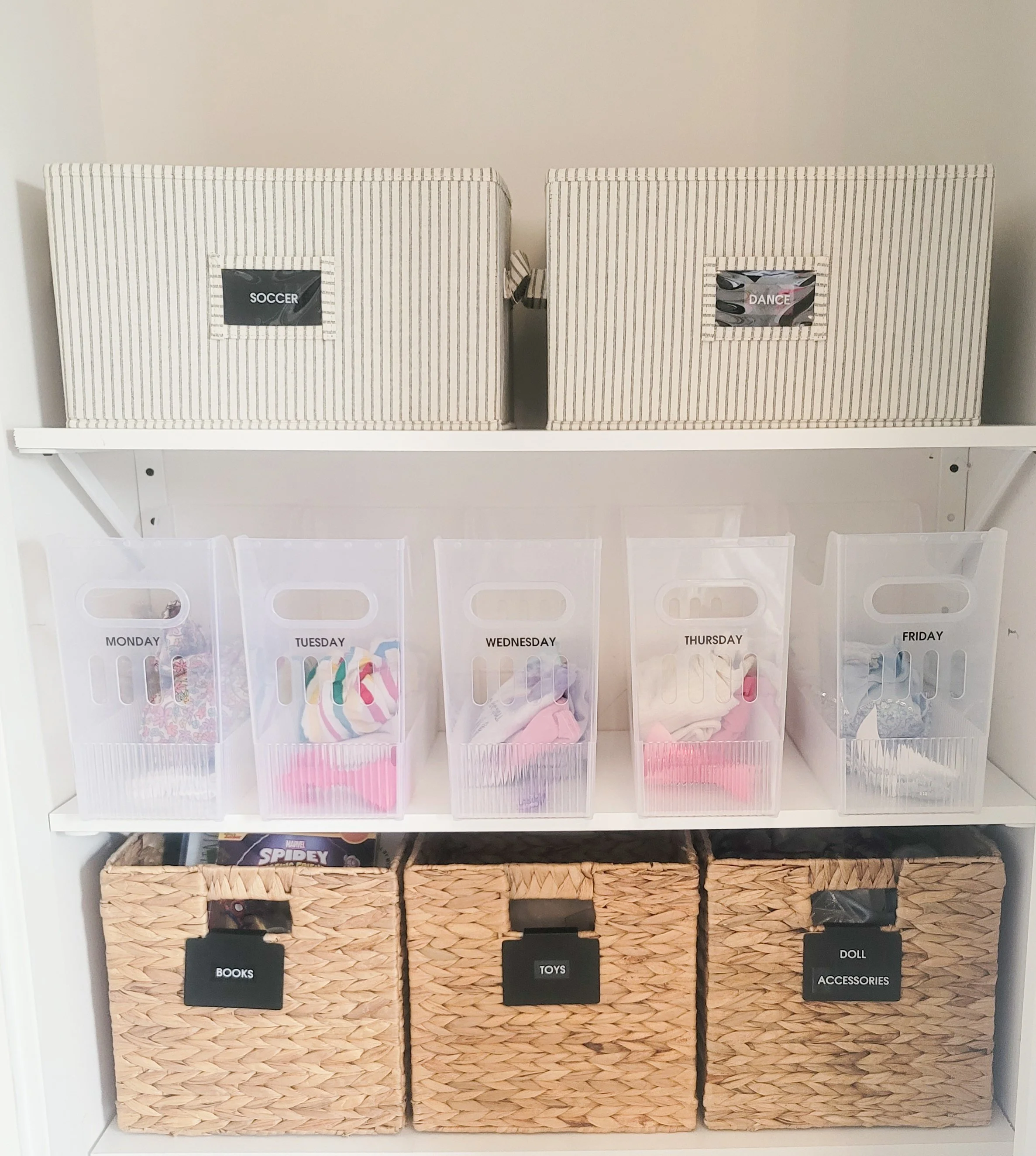 Organized kids closet with labeled weekday clothing bins, woven storage baskets, and labeled fabric bins for sports gear and toys.