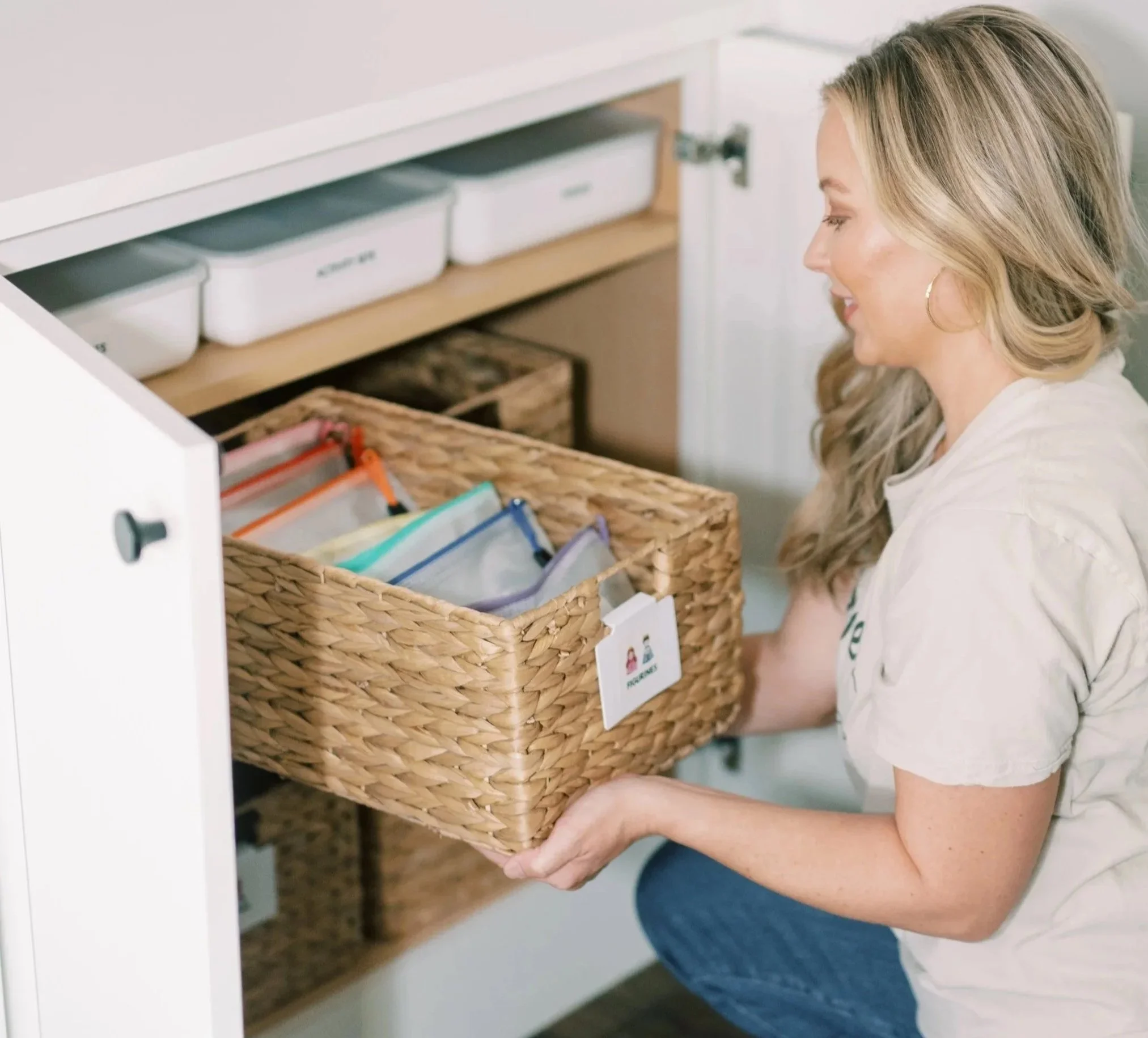 Professional organizer placing a labeled storage basket into an organized cabinet as part of a custom home organization system.