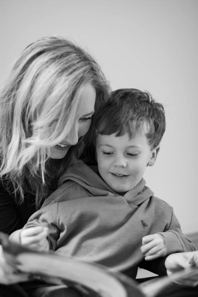 A woman and a boy sitting together, looking at a book with smiles on their faces.