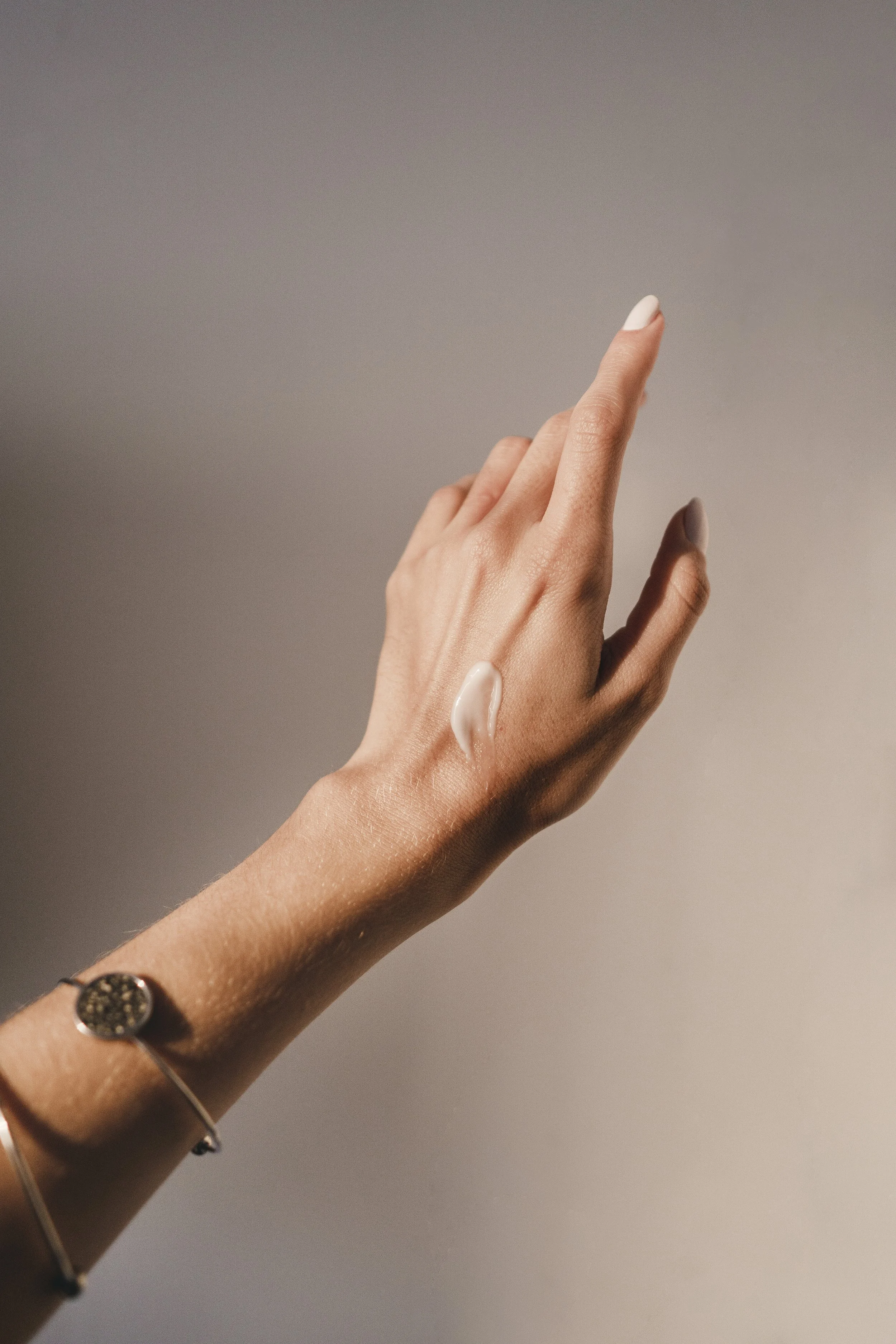 A person's hand with a piece of lotion on the back, wearing a bracelet, against a plain background.