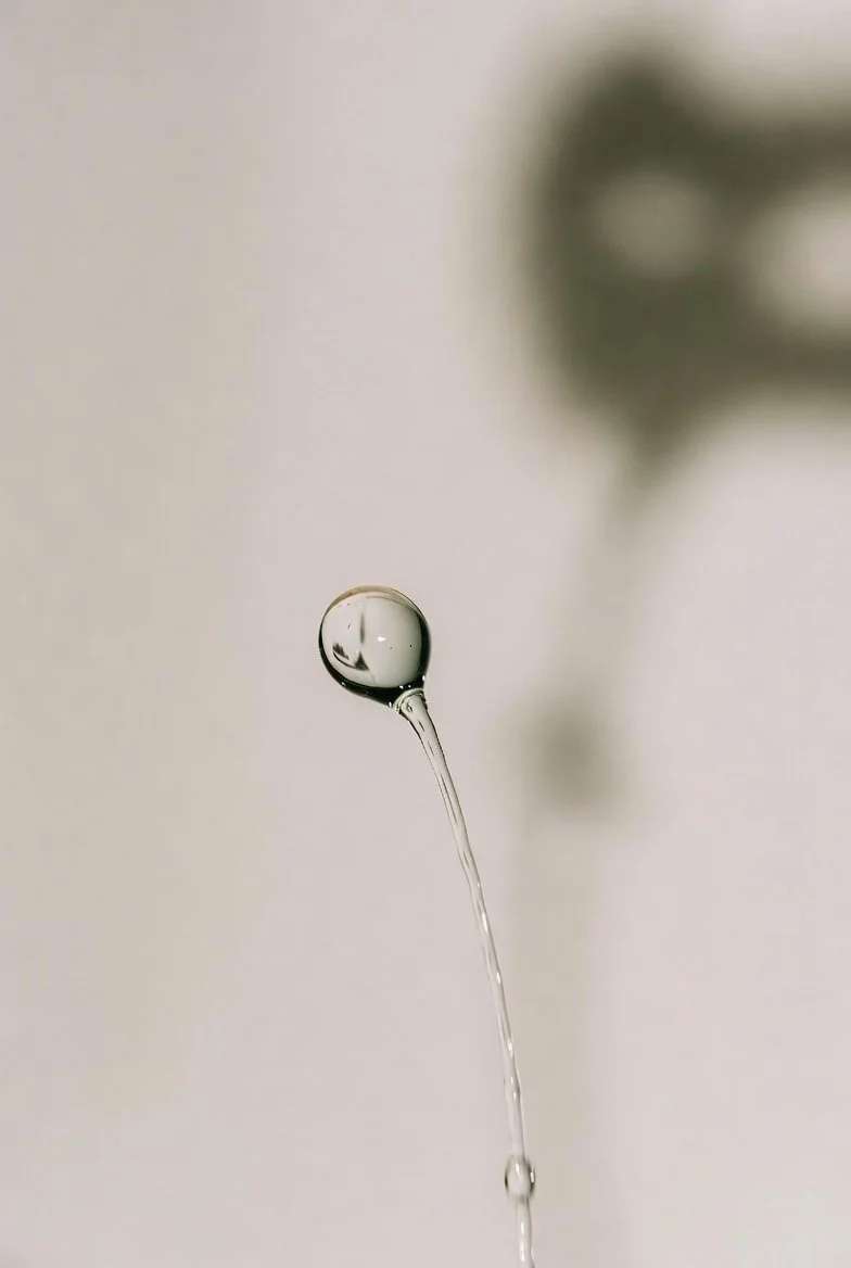 Close-up of a water droplet falling from a thin stream of water.