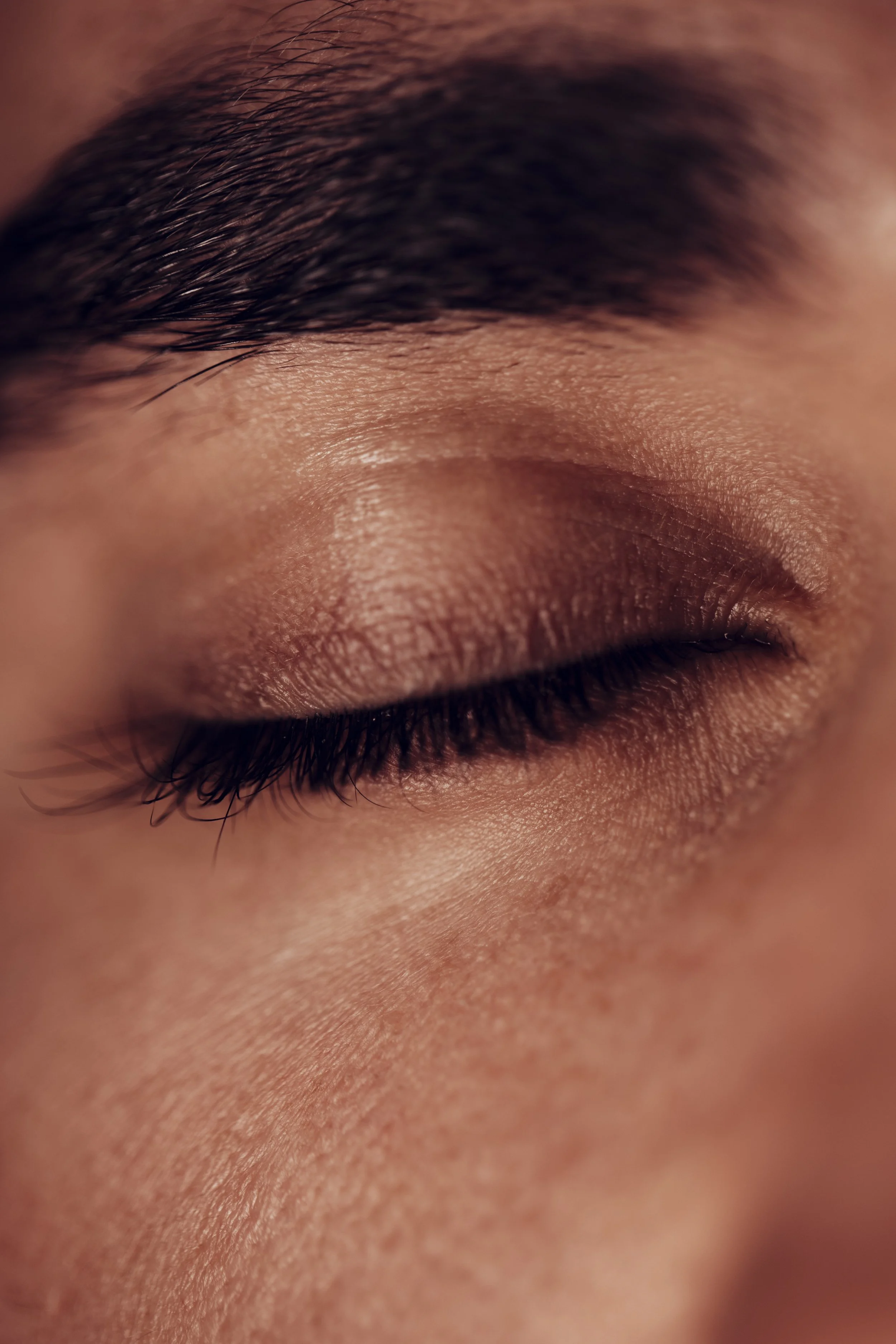 Close-up of a person's closed eye, showing detailed skin texture, eyelashes, and eyebrow.