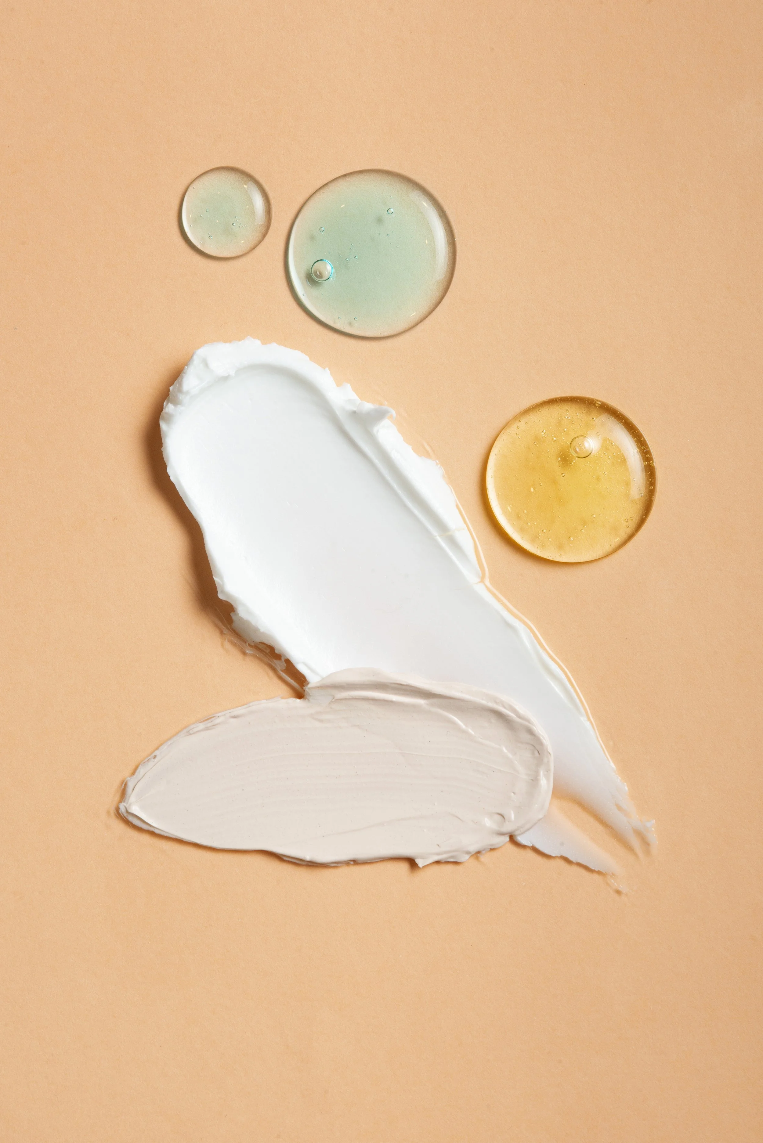 Creams or liquids in green, yellow, white, and beige colors on a peach background.