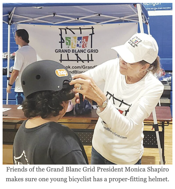 Grand Blanc Grid event with Monica Shapiro adjusting a helmet on a young bicyclist's head.