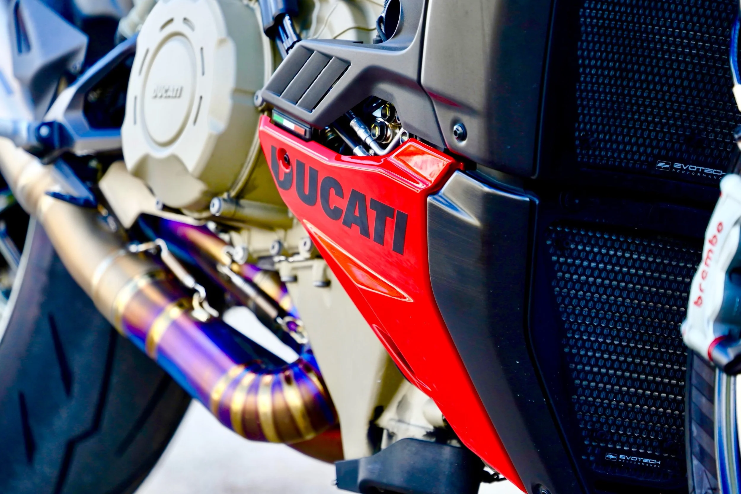Close-up of a Ducati motorcycle engine and frame, showcasing the red Ducati logo, metallic exhaust pipes, and various mechanical components.