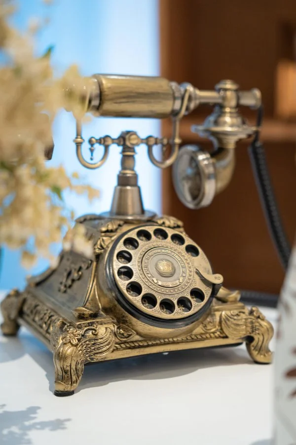 A vintage, antique-style telephone with a brass finish and ornate design details on a white surface, with blurred background.