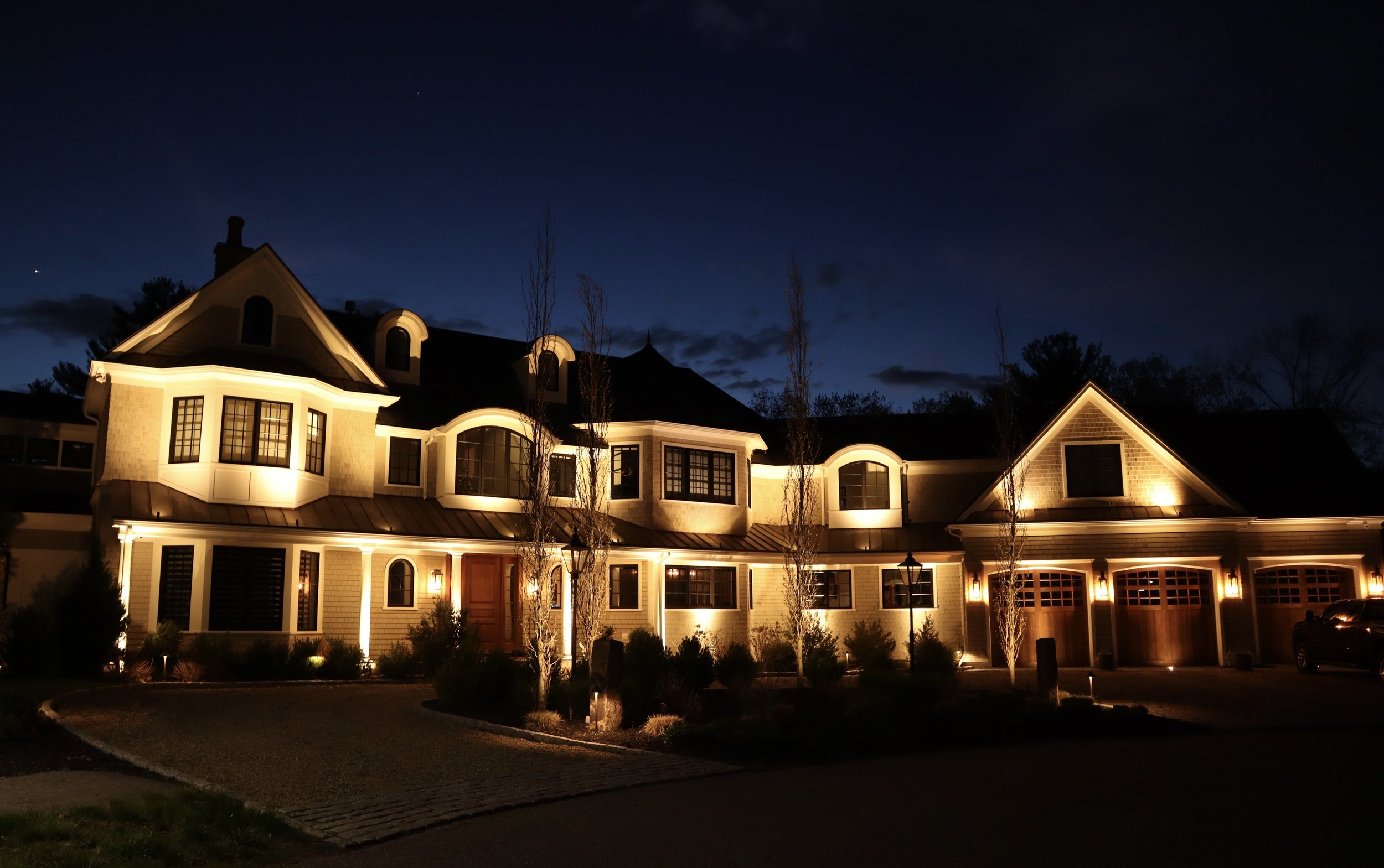 Architectural facade lighting accenting rooflines, dormers, and entry features on a custom home in Middleton, Massachusetts