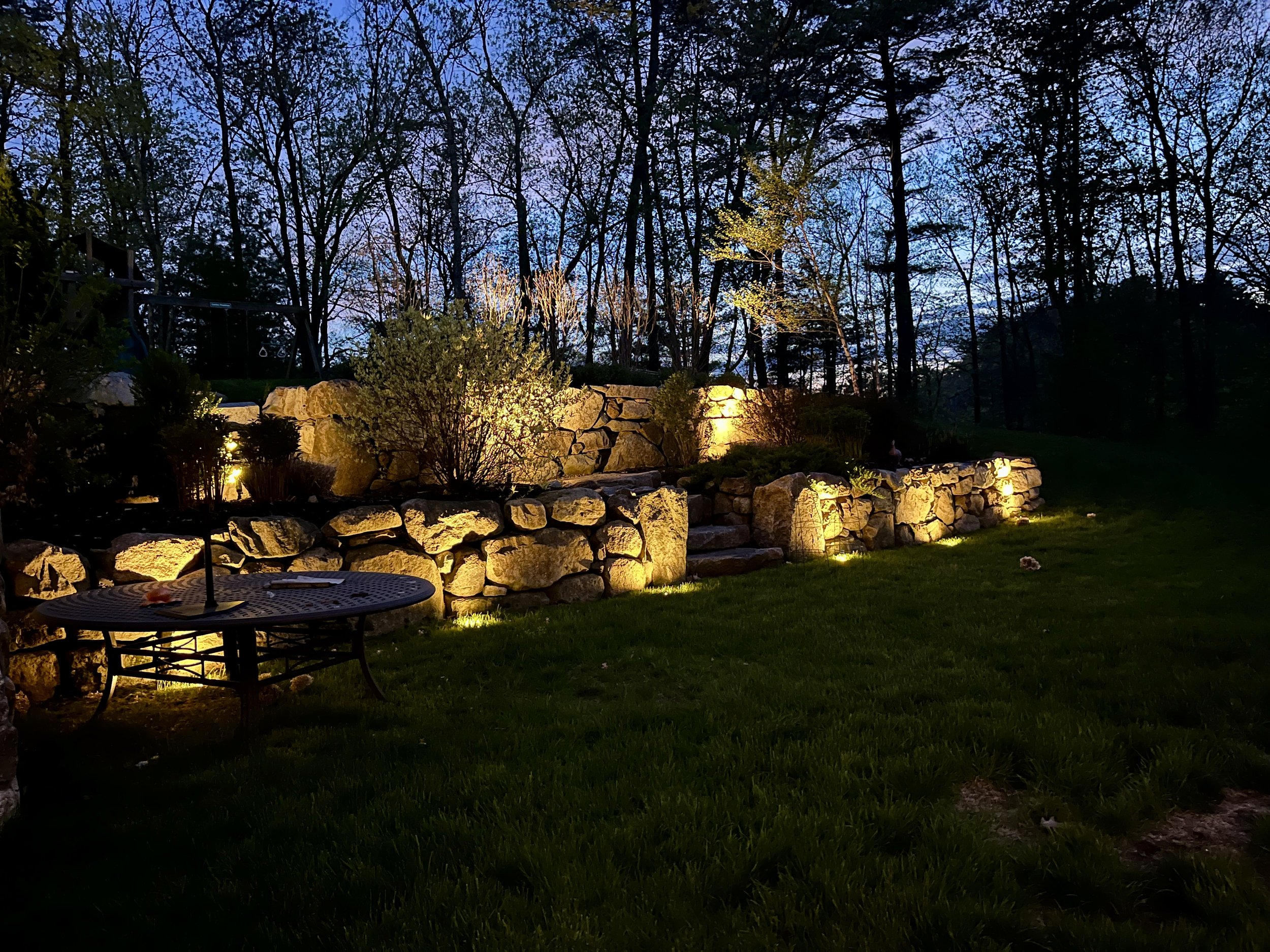 Landscape lighting illuminating natural stone retaining walls and planting beds at a Middleton residence
