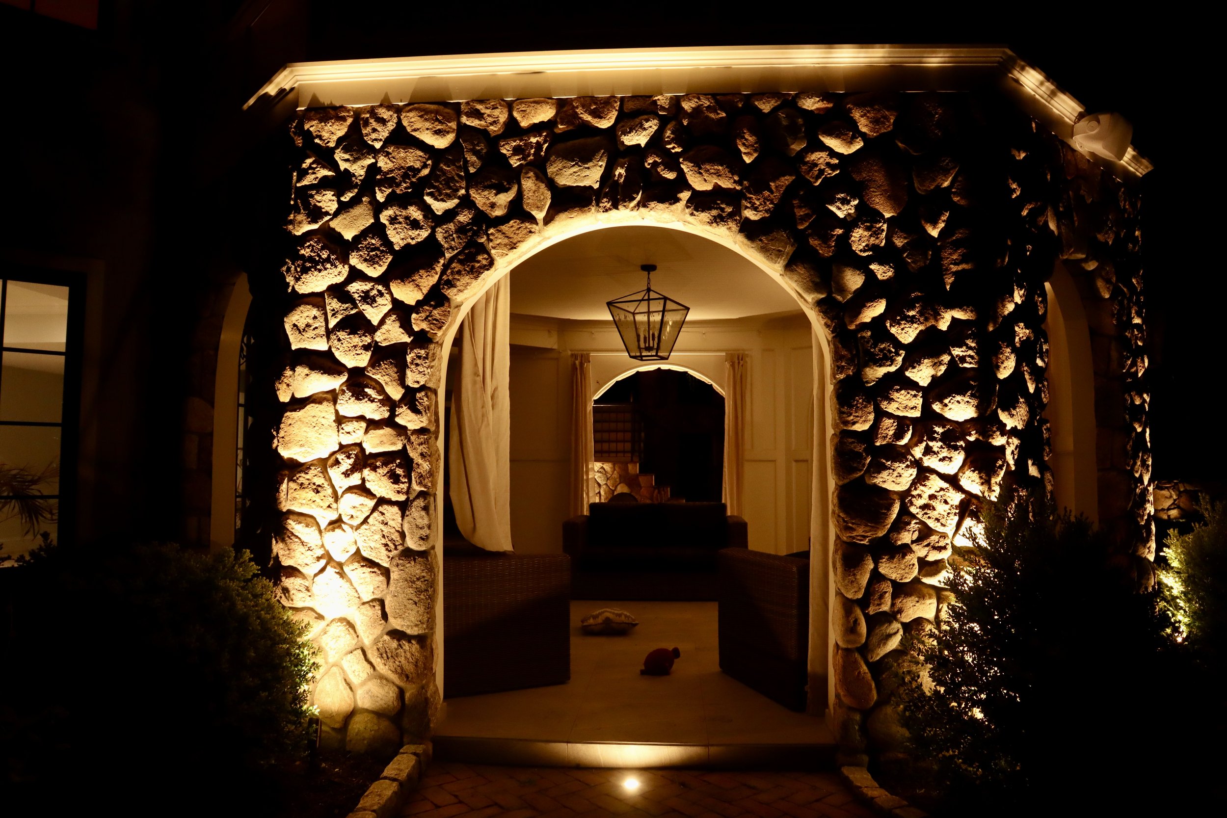 Outdoor lighting highlighting natural stone columns and integrated linear lighting beneath a covered patio in Middleton, MA