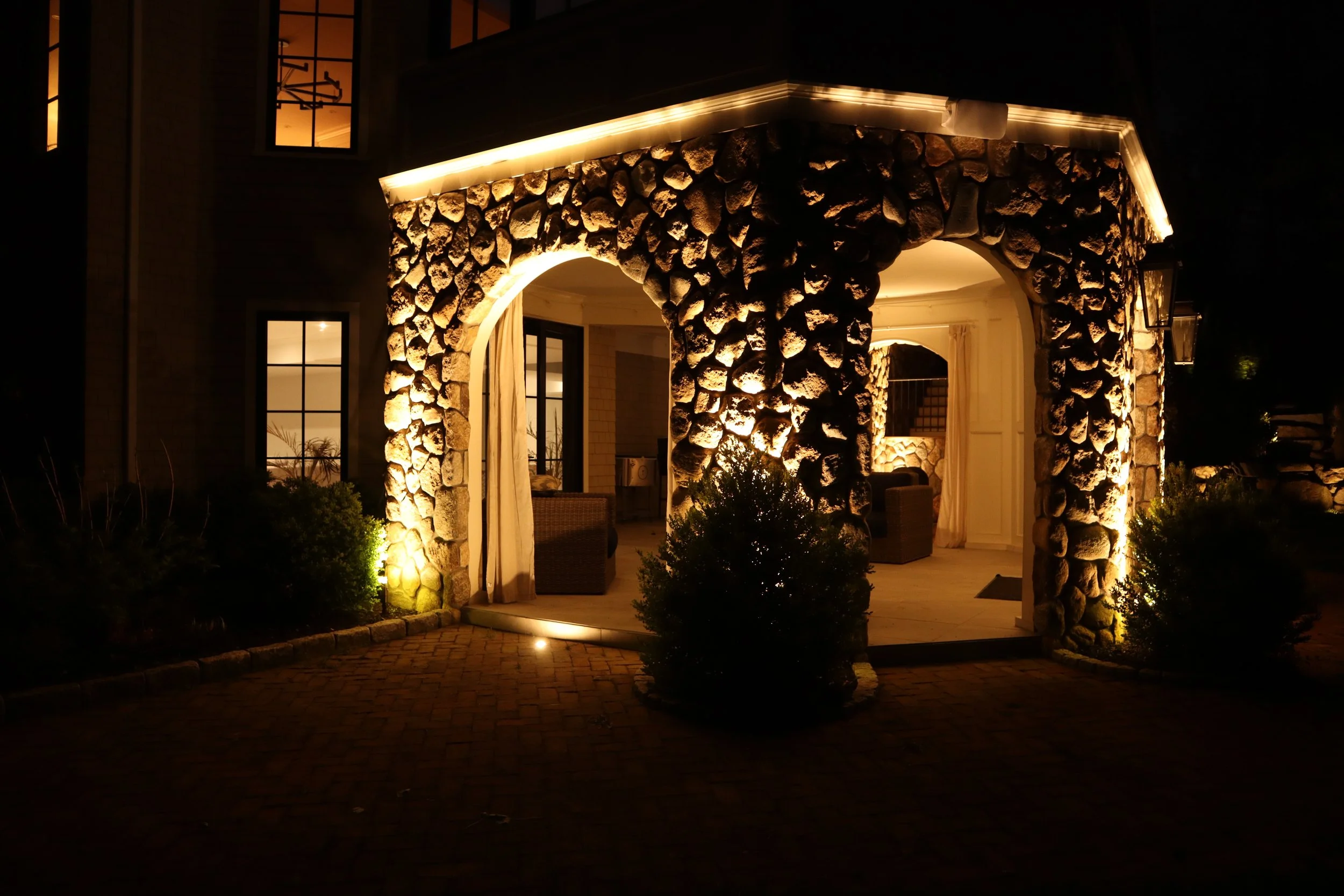 Outdoor lighting highlighting natural stone columns and integrated core drilled lighting beneath a covered patio in Middleton, MA