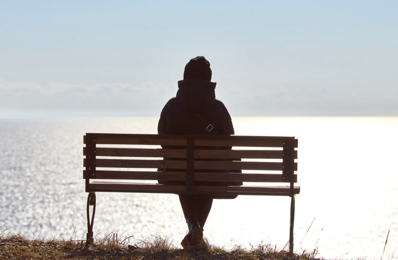 Person sitting alone on a bench at a lake, navigating loneliness