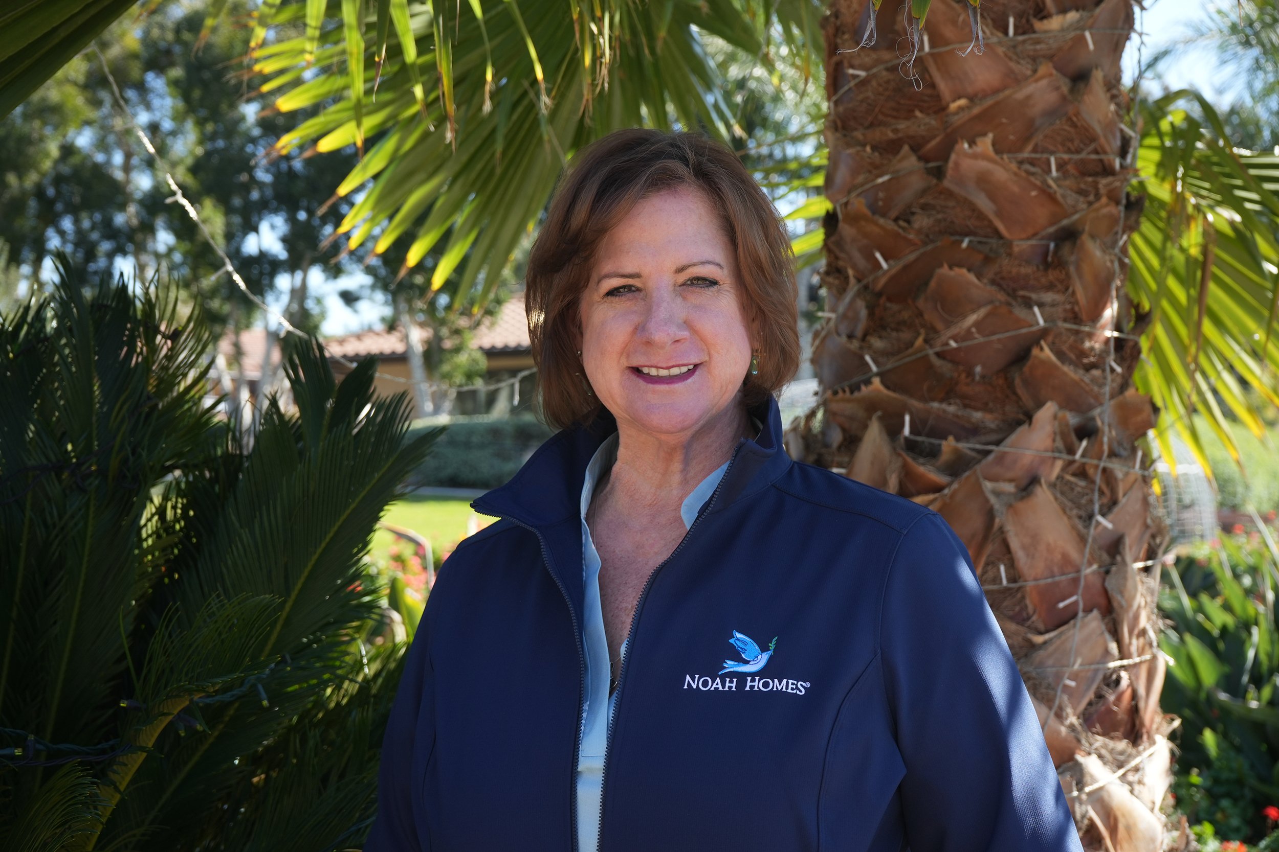 Woman in a blue jacket smiling in front of palm tree