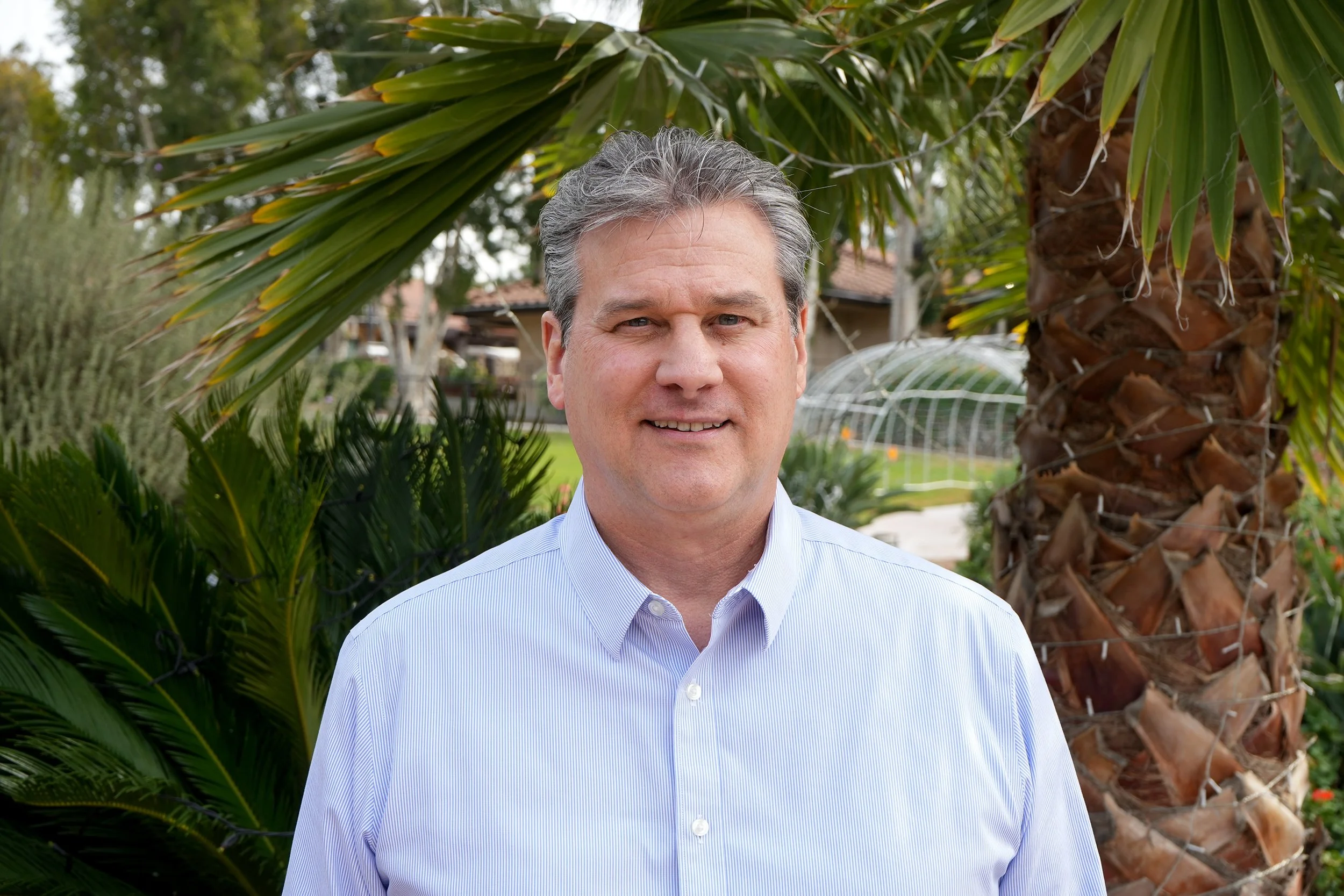 Man in button up shirt in front of palm tree