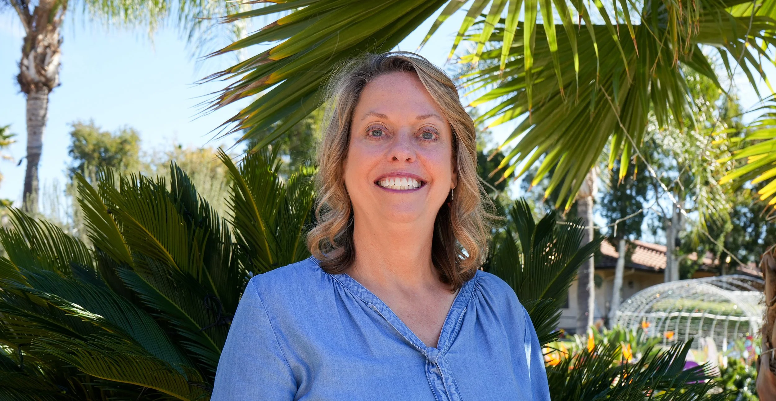 Woman in blue blouse smiling in front of palm tree