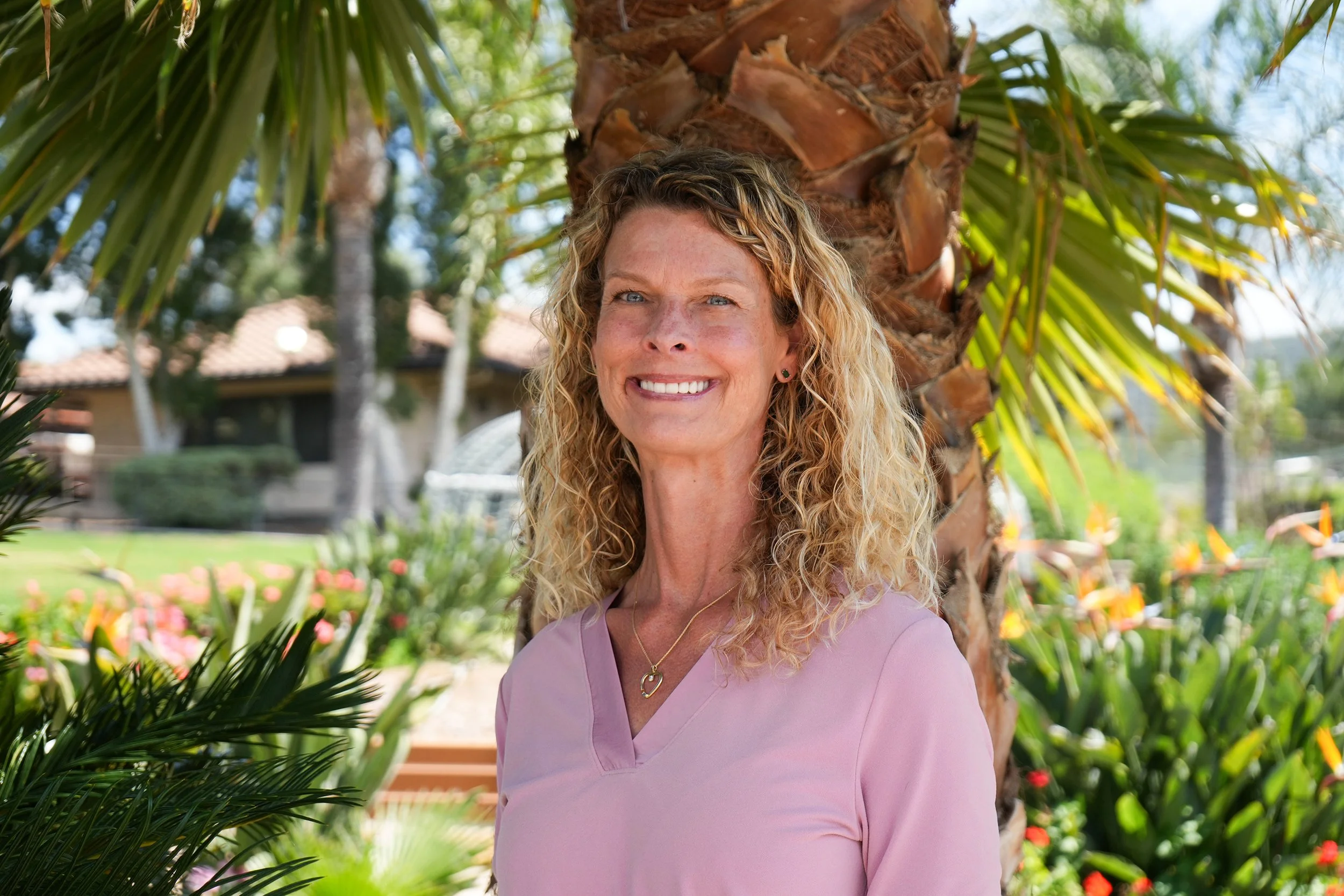 Woman in a pink blouse smiling in front of palm tree