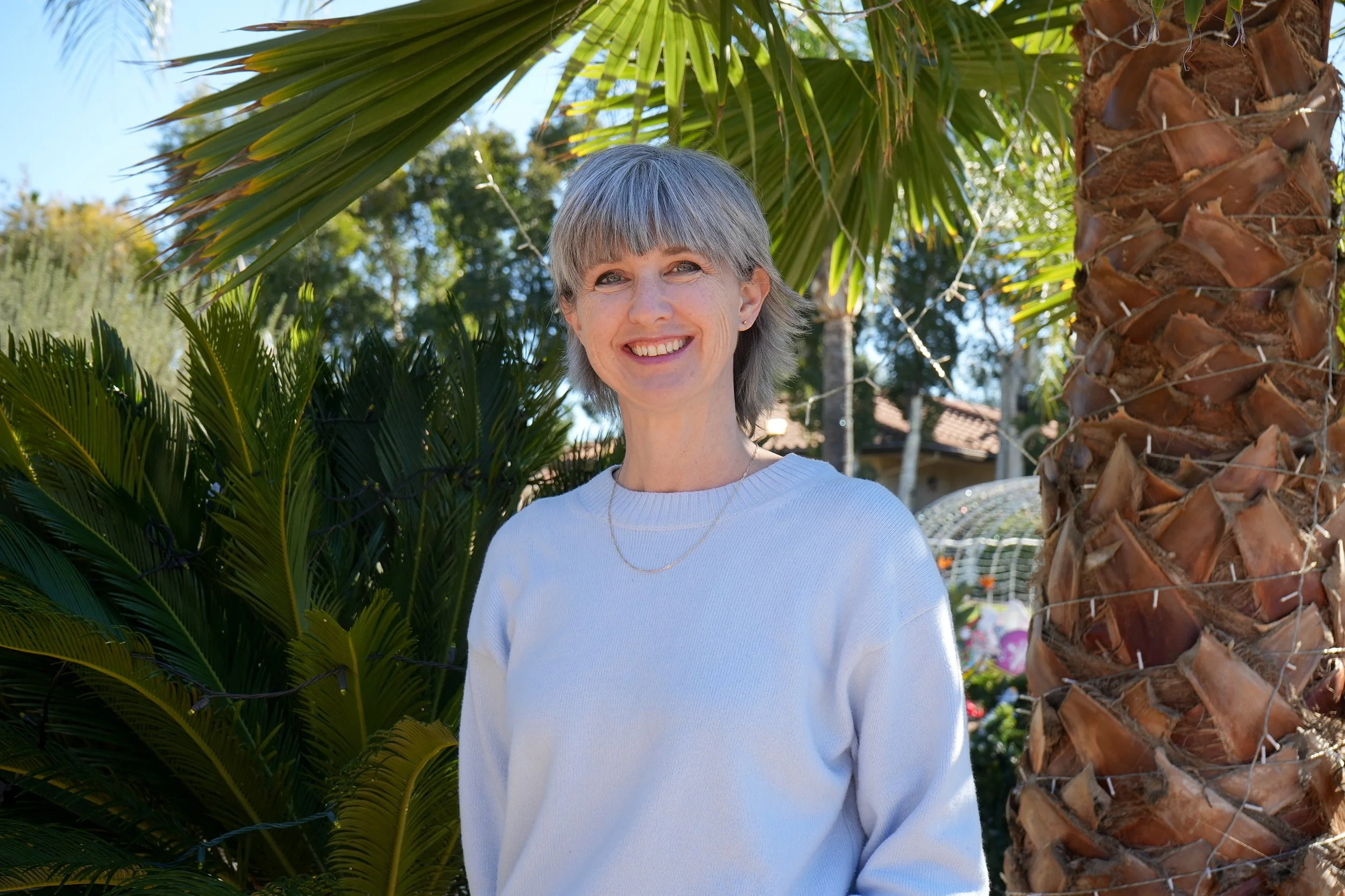 Woman in blue sweater smiling in front of palm tree