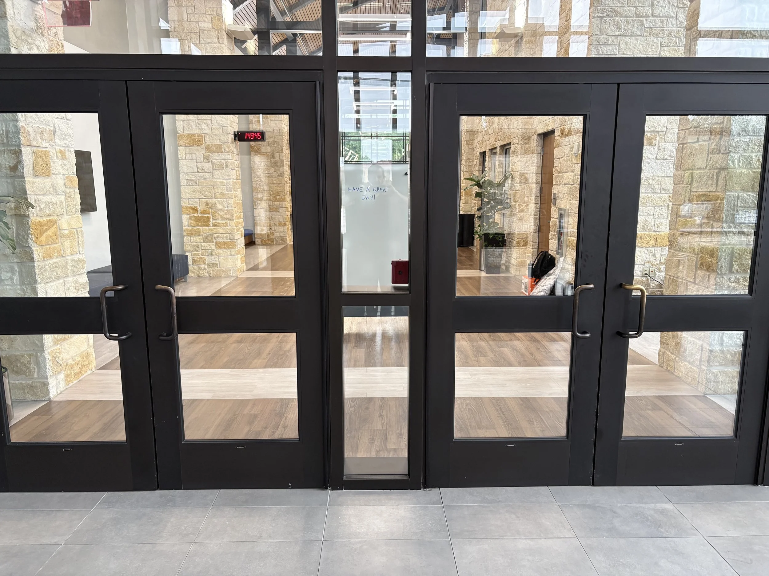 Corporate office vestibule with glass entrance doors and a Titan Armored TAG Mobile™ ballistic mobile whiteboard, rated UL 752 Level 8 and NIJ Level III.