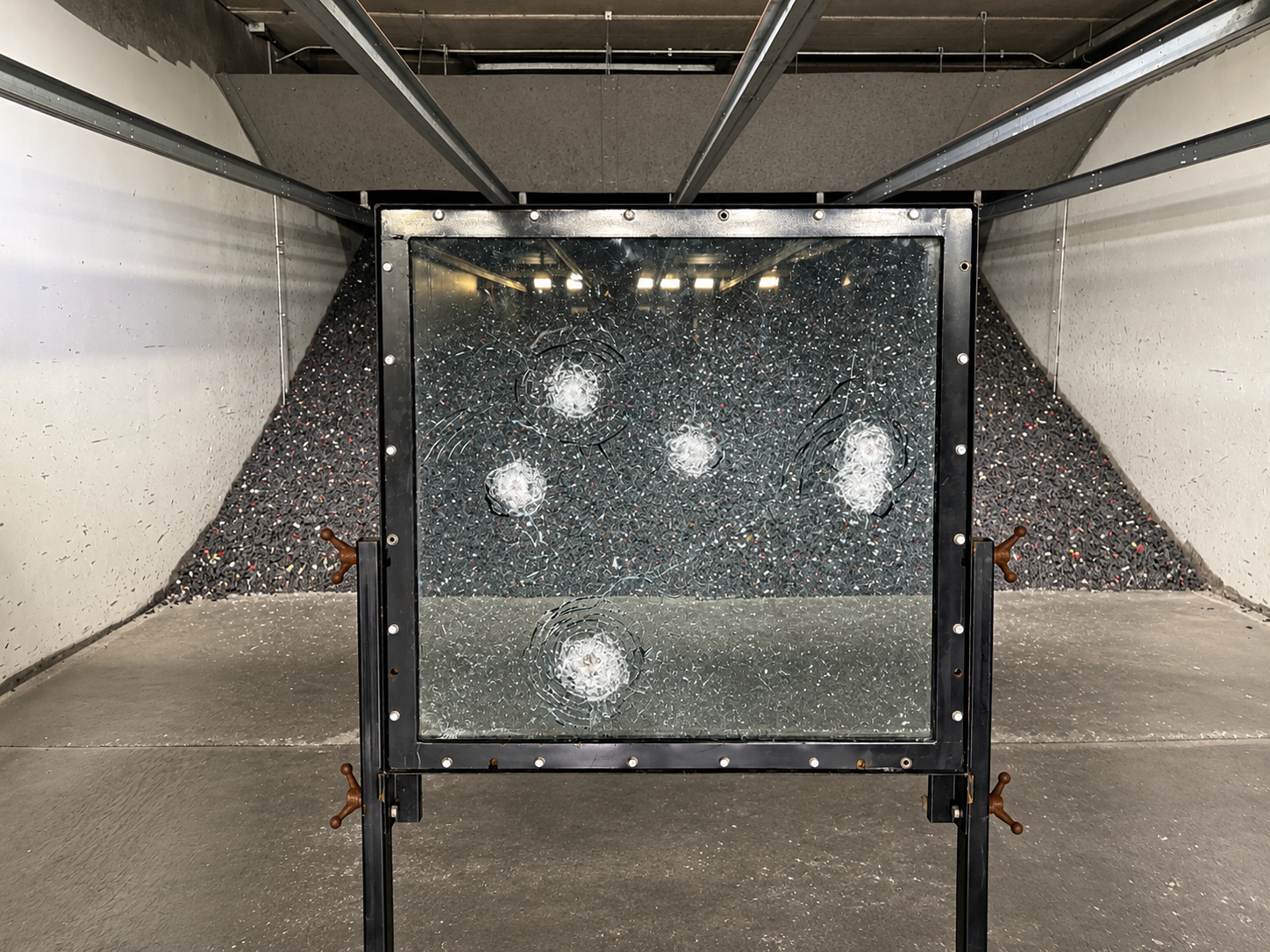 NIJ Level IIIA ballistic glass demonstration panel with visible projectile impact marks inside an indoor ballistic testing range.