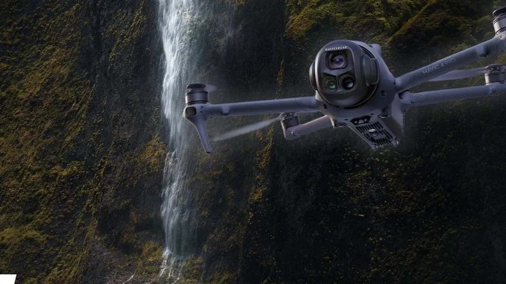 A drone flying near a waterfall in a lush green landscape.