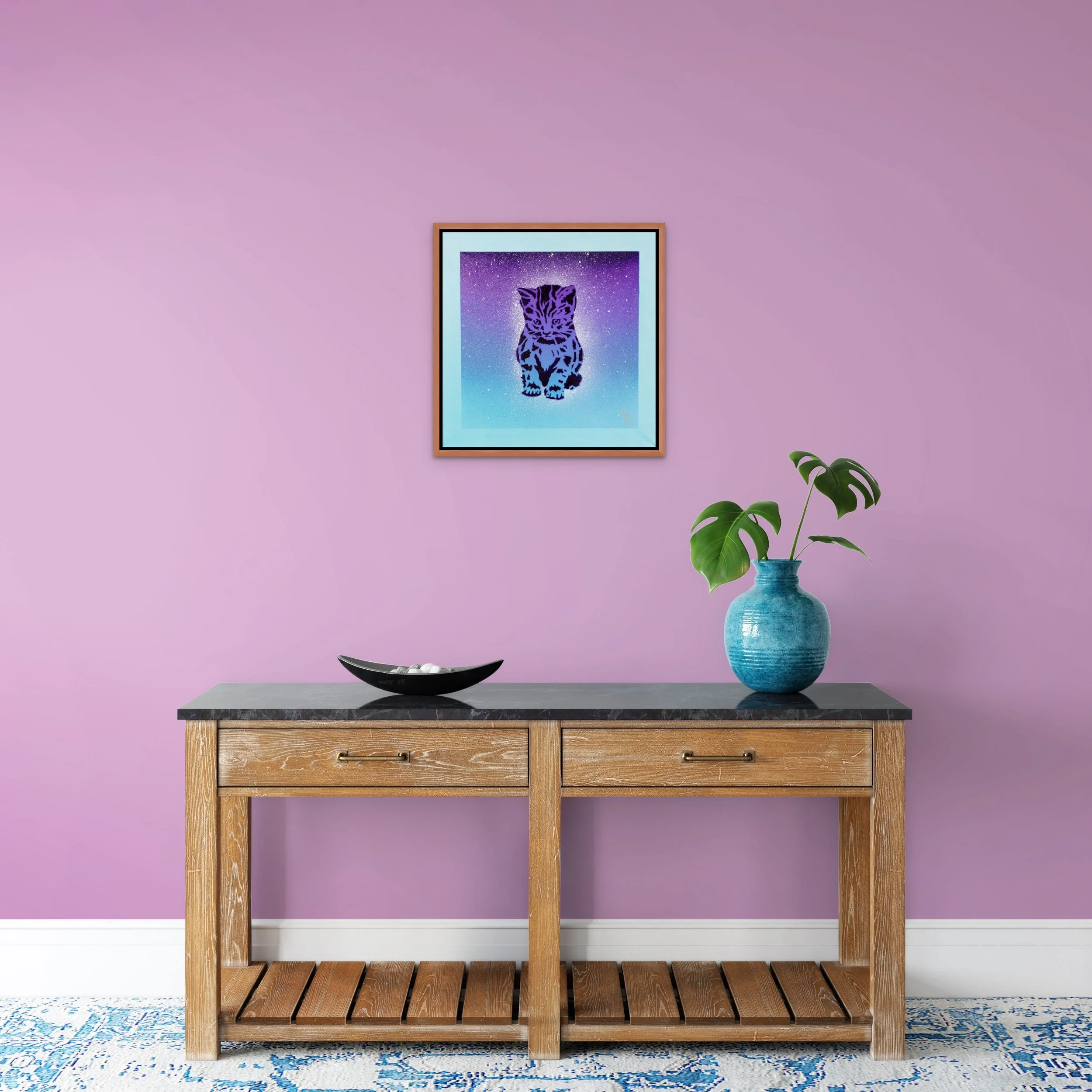 A wooden table with a black bowl and a vase with green leaves against a purple wall with framed artwork depicting a tiger and galaxy, and a blue patterned area rug.