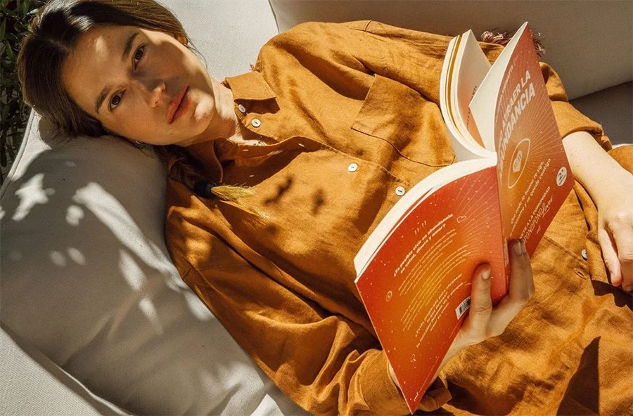 Lifestyle portrait of a woman reading in sunlight, reflecting the calm, grounded aesthetic behind the Reverie Residential brand direction.