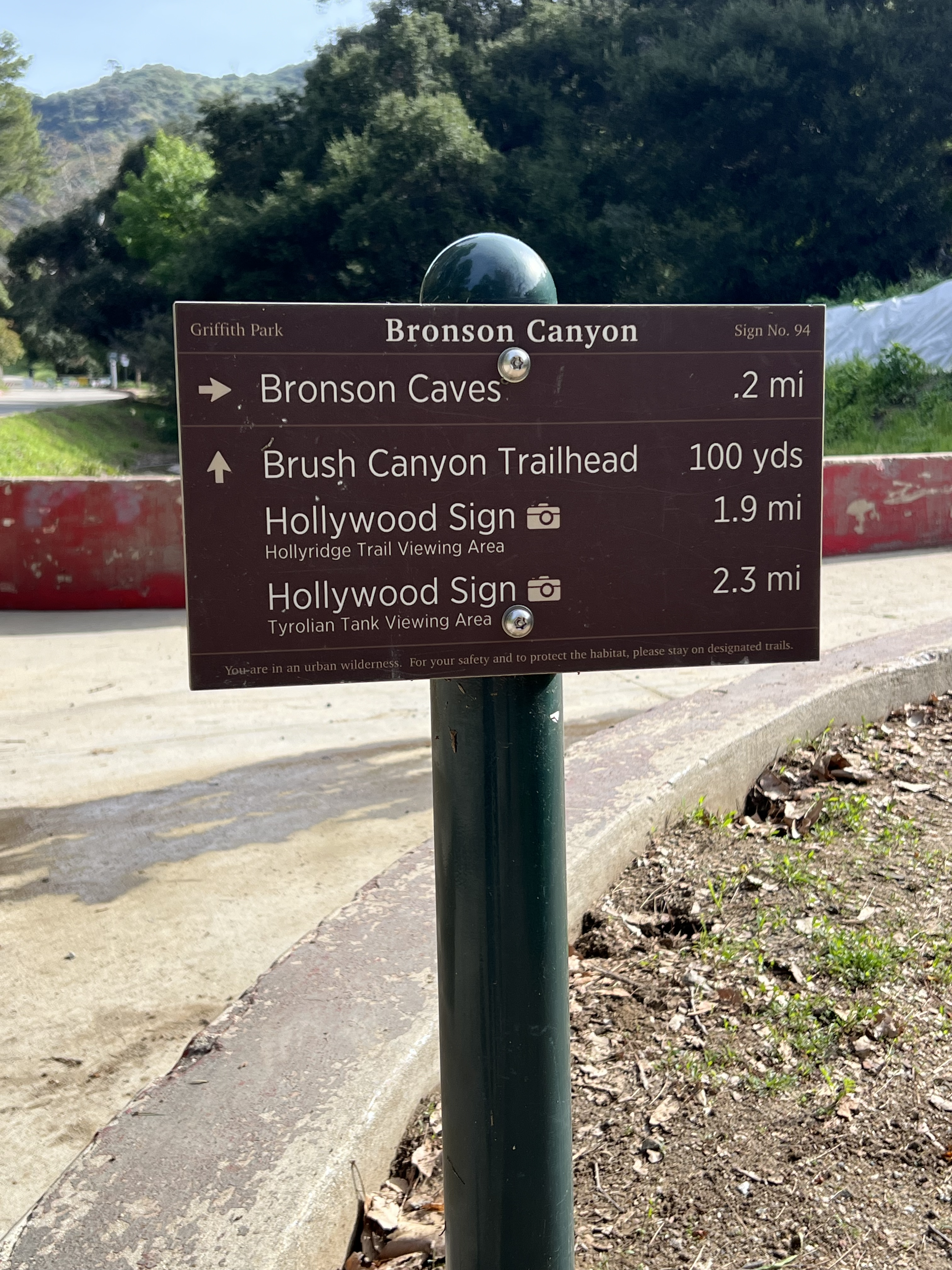 Trail sign in Griffith Park, Bronson Canyon, showing directions to Bronson Caves, Brush Canyon Trailhead, and the Hollywood Sign with distances.