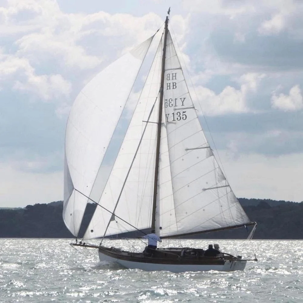 A sailboat with white sails on a body of water, with a cloudy sky and distant shoreline in the background.