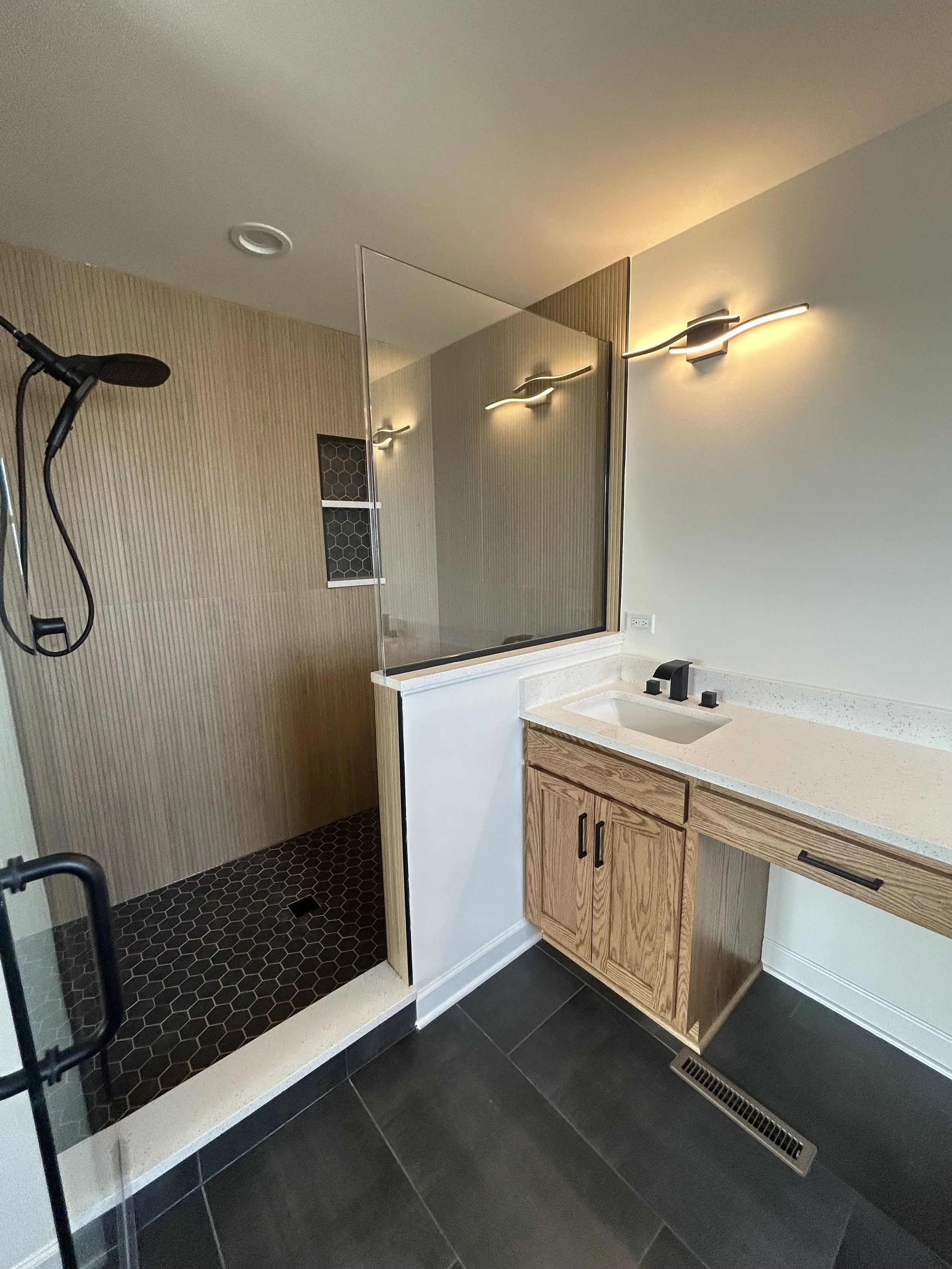 Bathroom with a walk-in shower that has a glass wall, wooden cabinets, a black faucet, and dark floor tiles.
