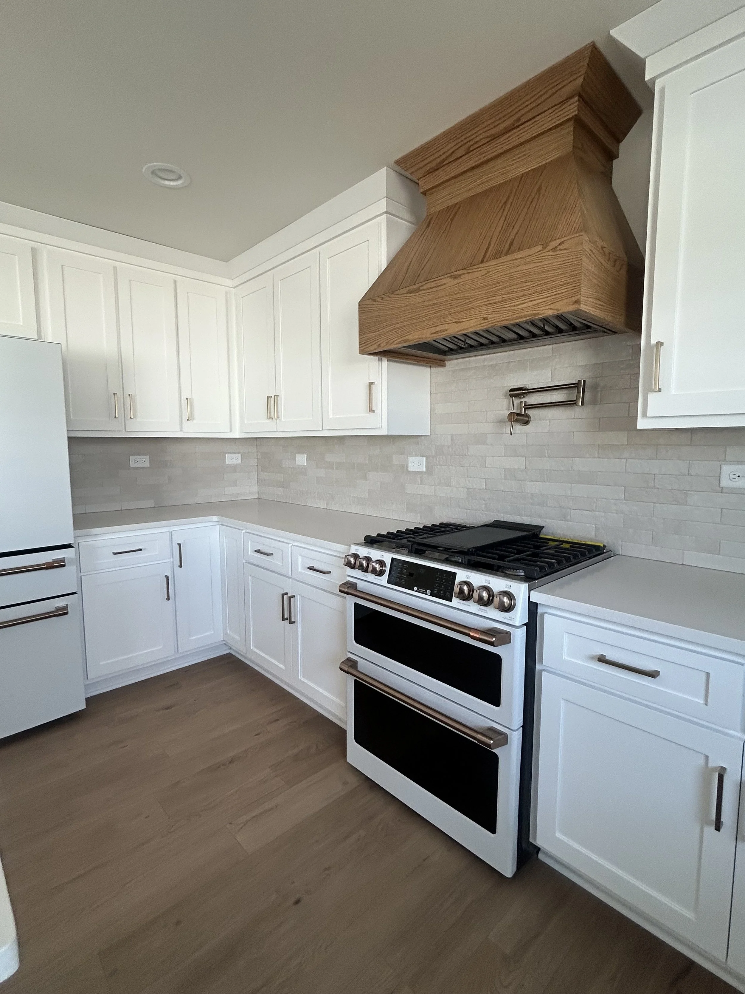 Modern kitchen with white cabinets, a white stove, a wooden range hood, light-colored brick backsplash, and hardwood floors.