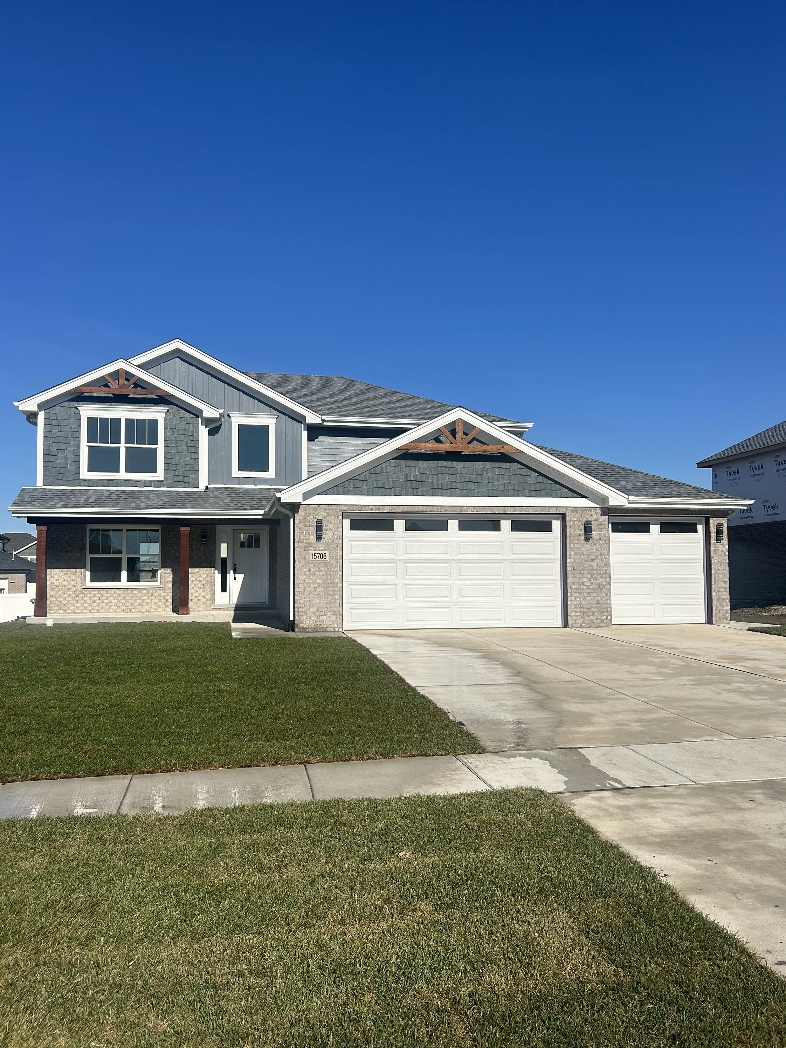 New two-story house with blue-gray siding, white trim, a three-car garage, and a well-maintained front lawn under a clear blue sky.