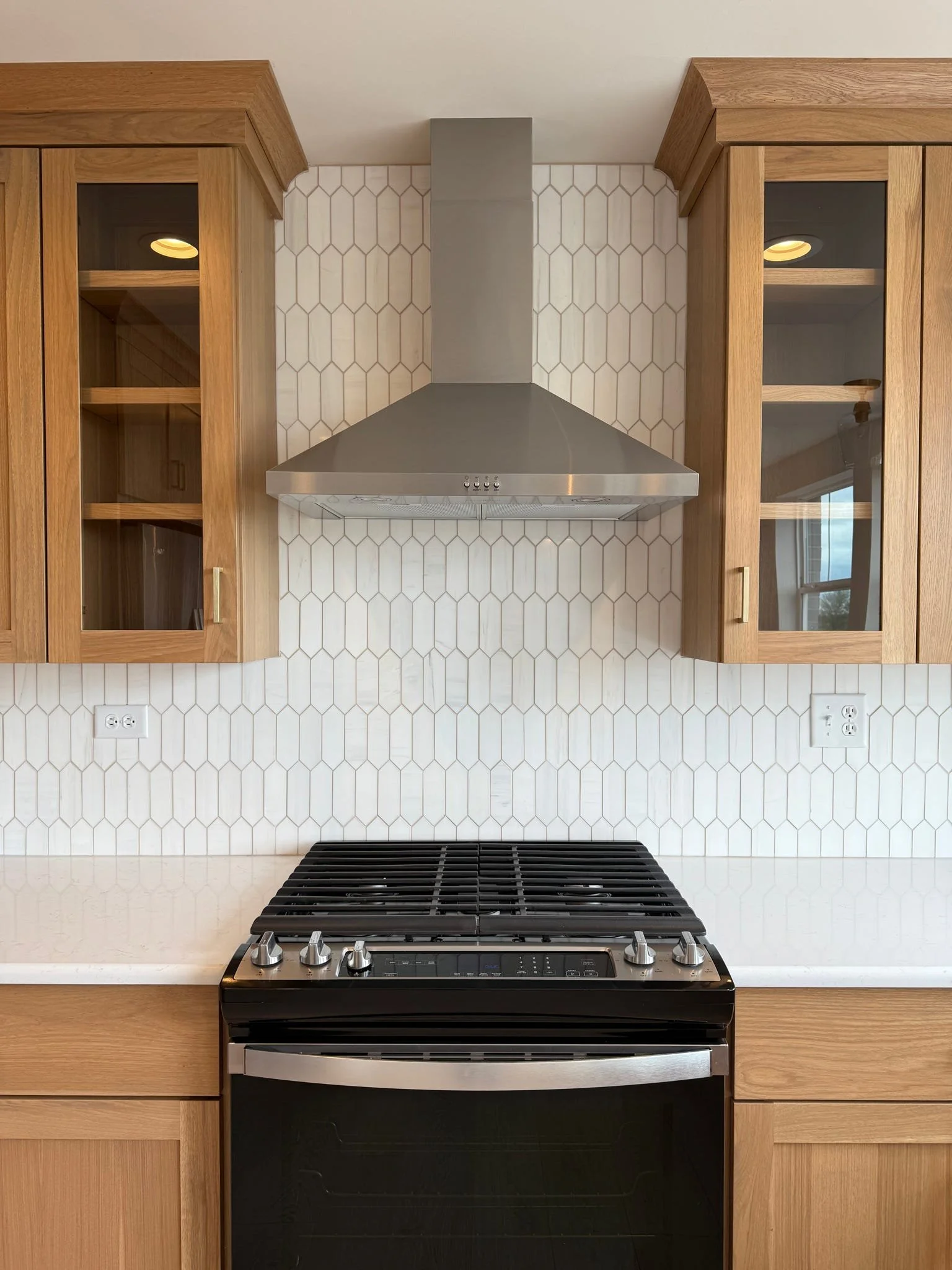 Kitchen with wooden cabinets, a stainless steel range hood, and a black stove in front of a white tile backsplash with a honeycomb pattern.