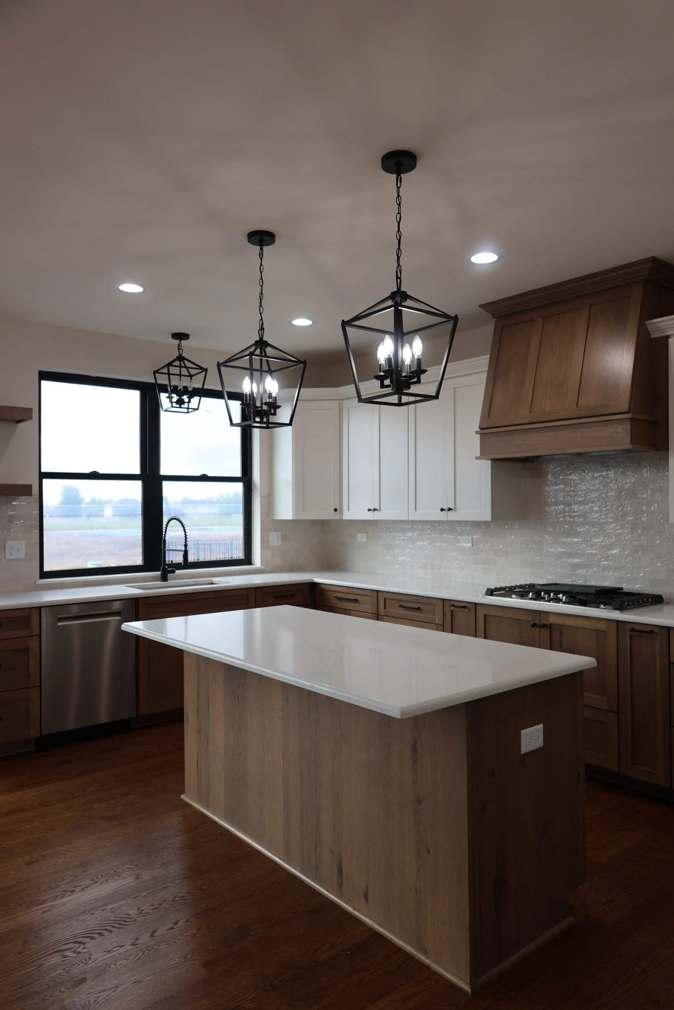 Modern kitchen with white and wooden cabinetry, a center island with a white countertop, a window above the sink, and three pendant lights hanging from the ceiling.