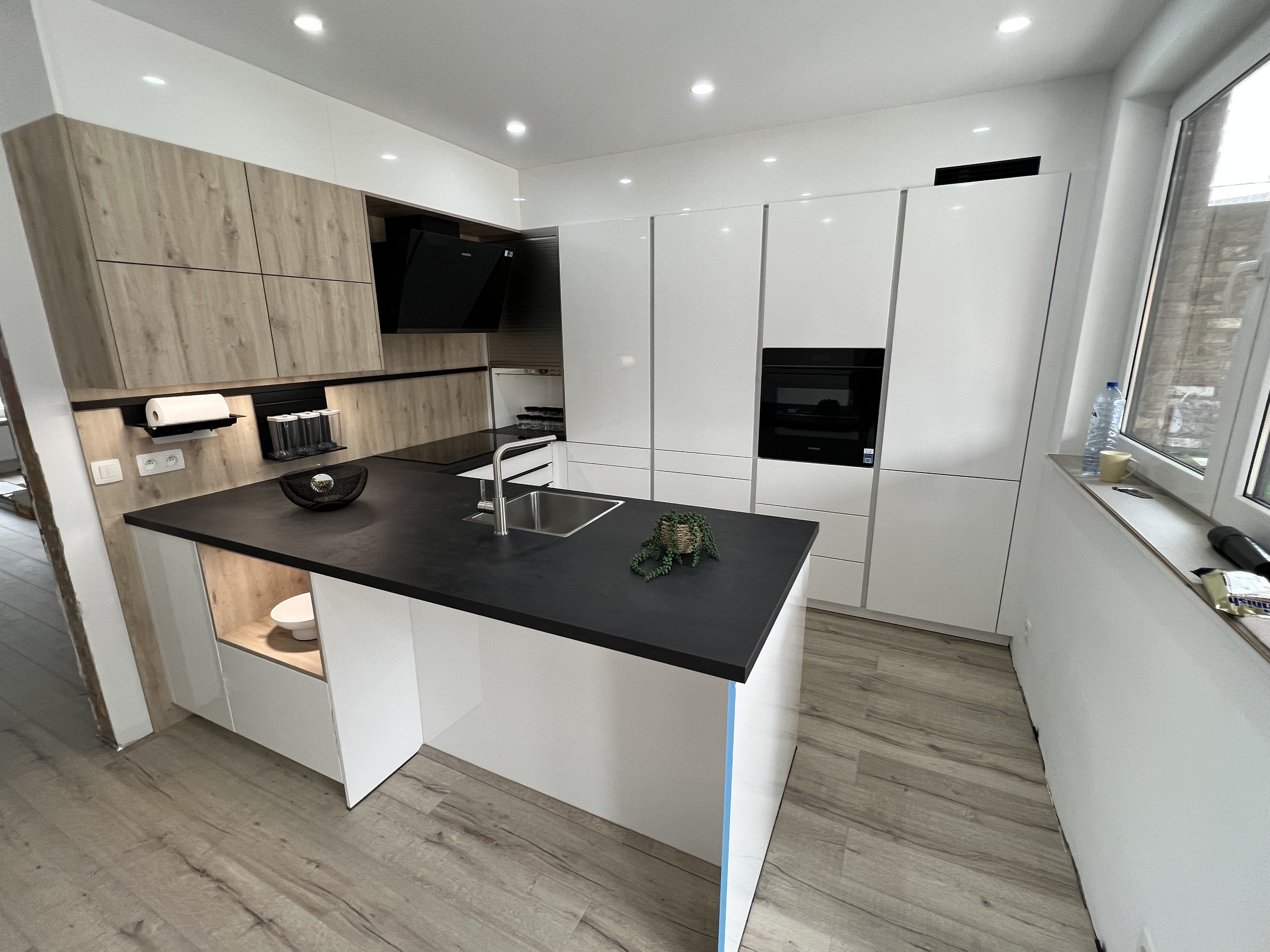 Modern kitchen with white cabinets, black countertop island, built-in oven, and window with bottle and cup on windowsill