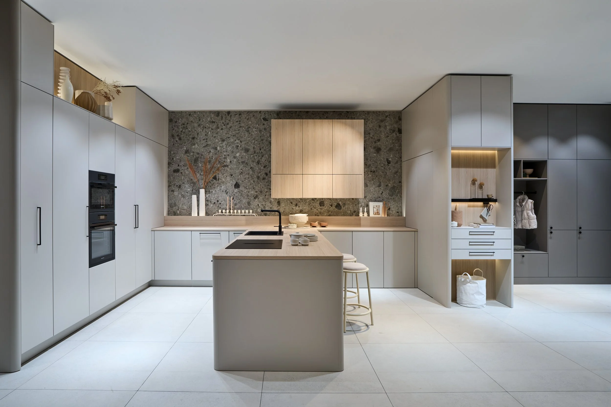 Modern kitchen with white cabinets, a central island with a built-in stove, a stone backsplash, wooden accents, and minimalist decor.