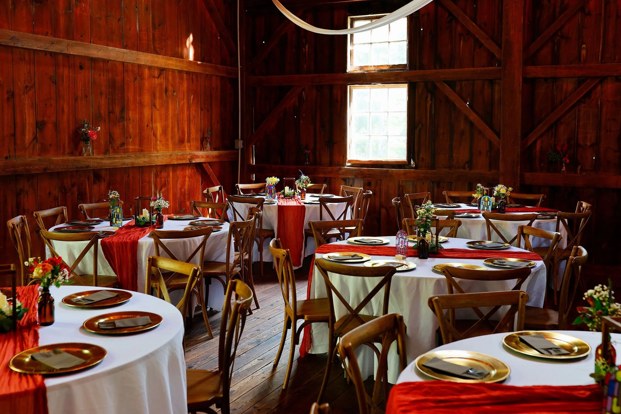 Wedding cake and other pastries on table with barn venue and guests in background