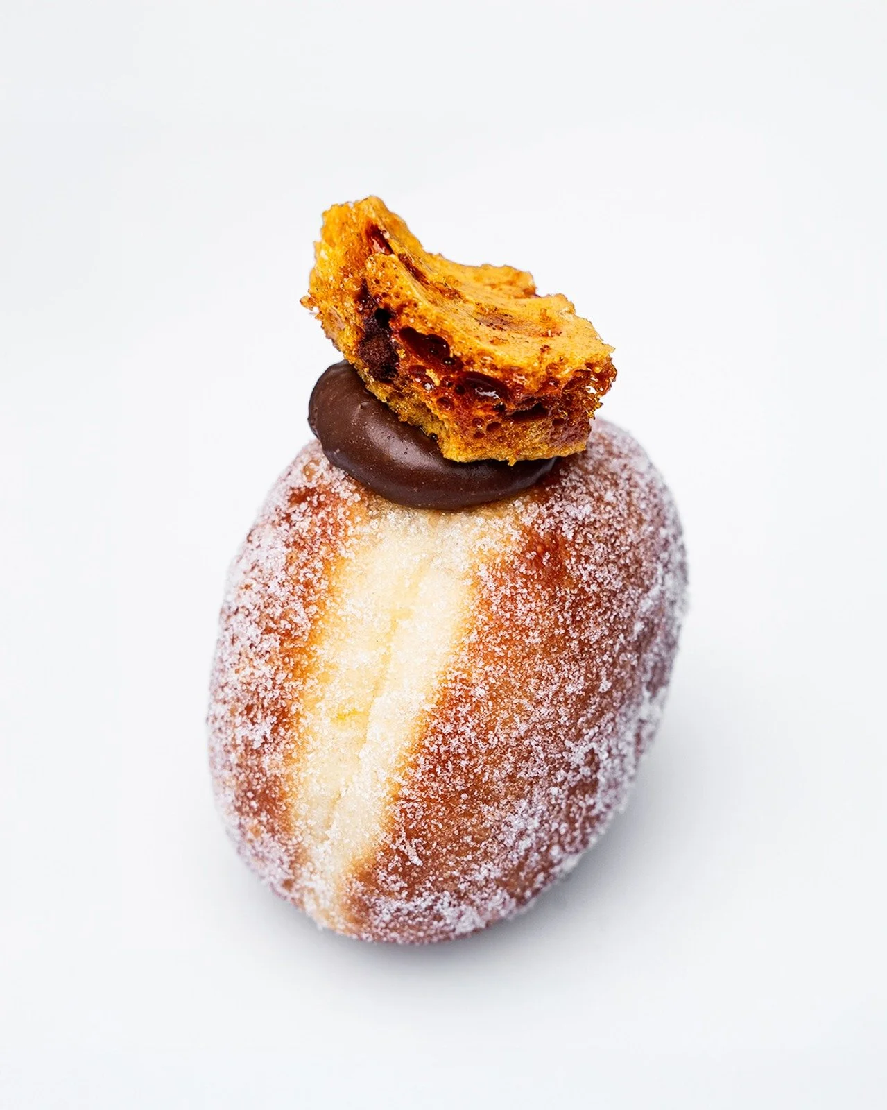 A cheeky chocolate filled doughnut on a plain white background, topped with a naughty chunk of cinder toffee. Chocolate is visibly bursting from the top.
