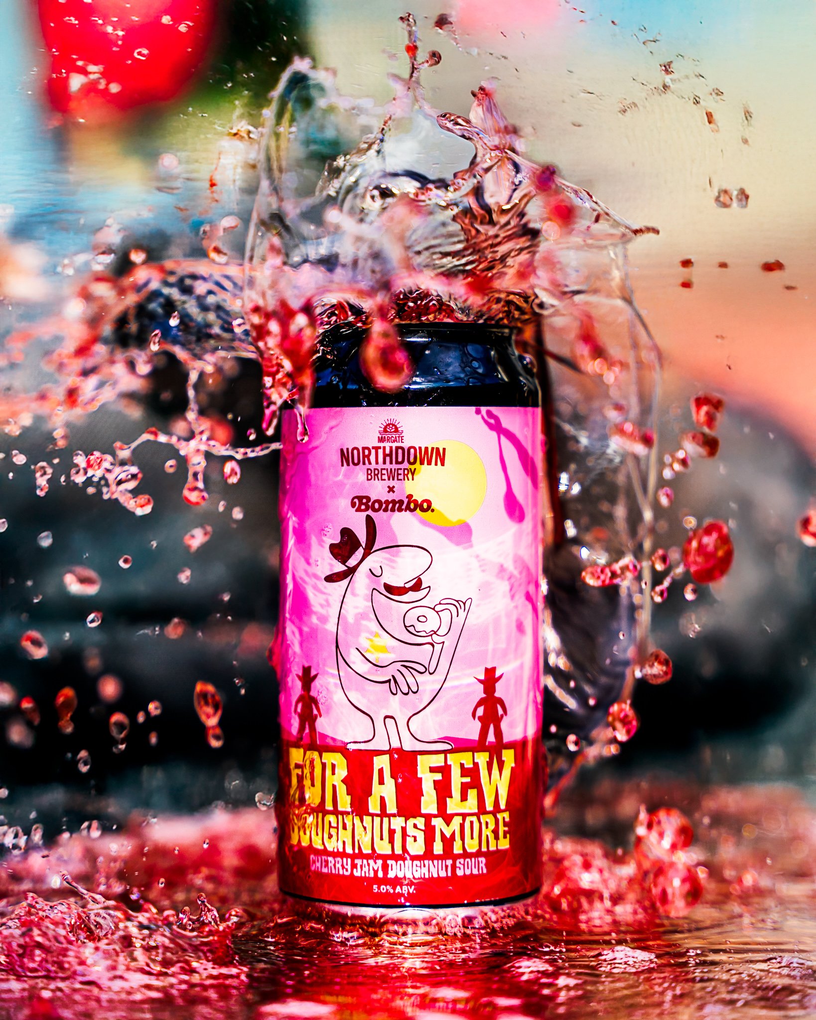 An image of a can of Bombo x Northdown Brewery collab beer. The can is sitting in a pool of red coloured cherry sour beer, red beer is poured from above and is splashing absolutely everywhere. It looks dramatic, but undoubtedly messy (and delicious)!