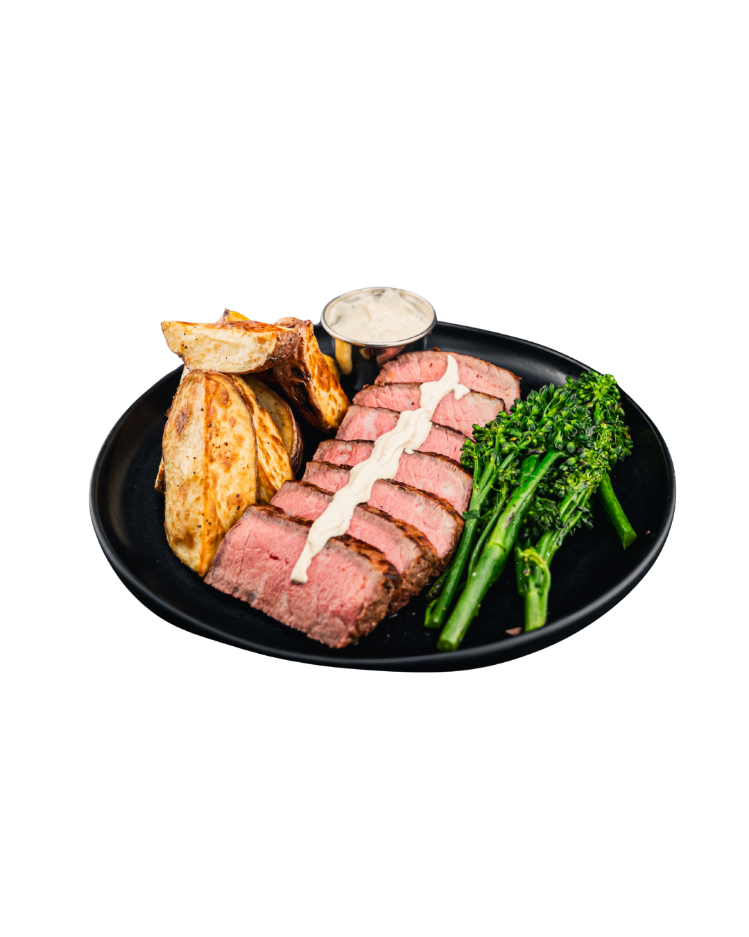 Plate with sliced steak, roasted potatoes, broccolini, and a side of creamy dipping sauce.