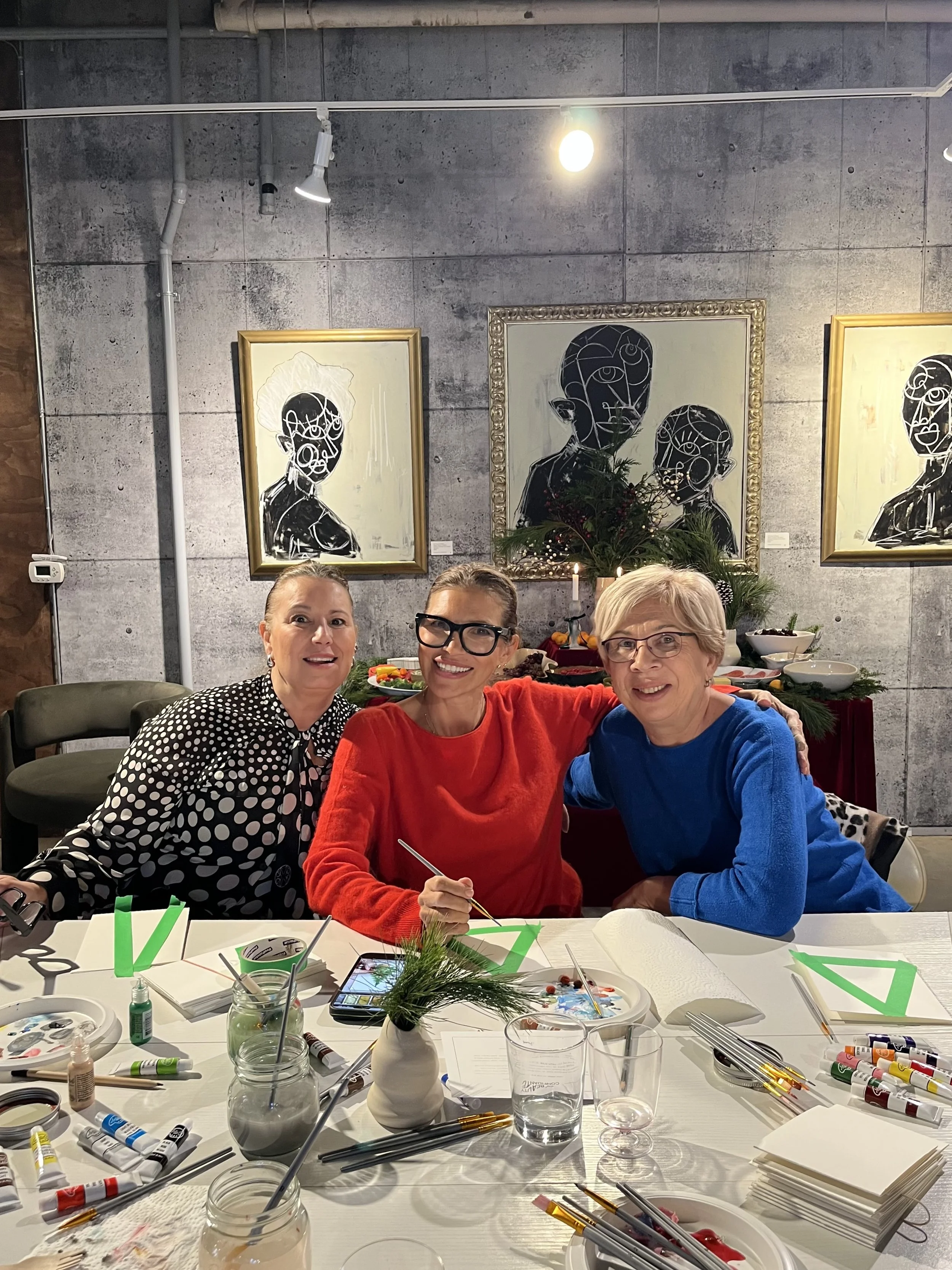 Three women sitting at a table decorated for Christmas, smiling and posing for a photo