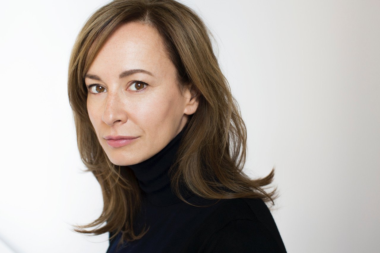 A woman with light skin and brown hair wearing a black turtleneck.
