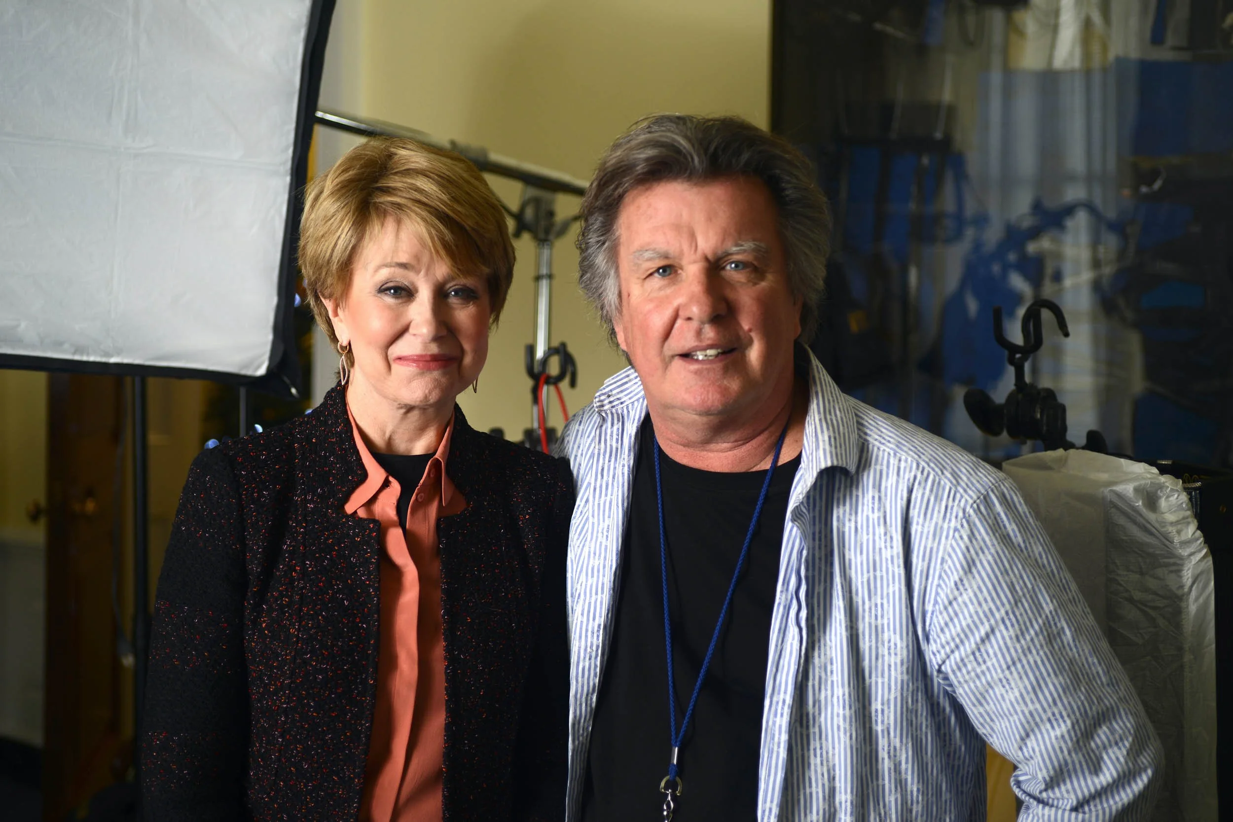 A woman and a man standing together in a photography studio, smiling at the camera.
