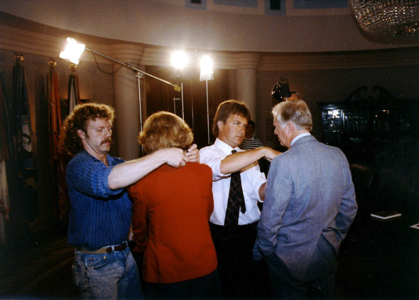 Four people in a photography studio engaged in a close discussion or interview, with studio lights and equipment visible in the background.