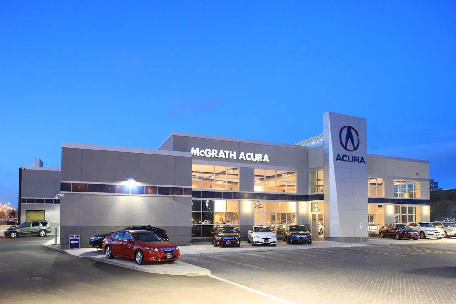 Exterior view of McGrath Acura car dealership during evening, with cars parked in front and illuminated signage.