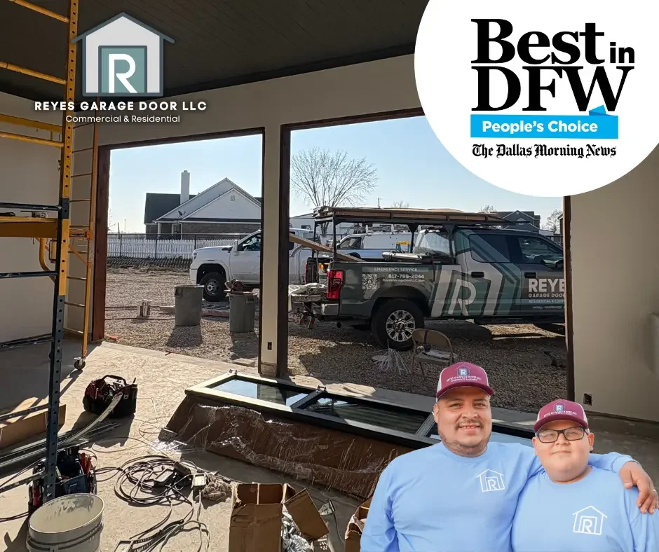 Inside a garage with construction equipment and materials, two men in matching blue shirts and maroon hats stand in the foreground, with a truck and house visible outside the garage window.