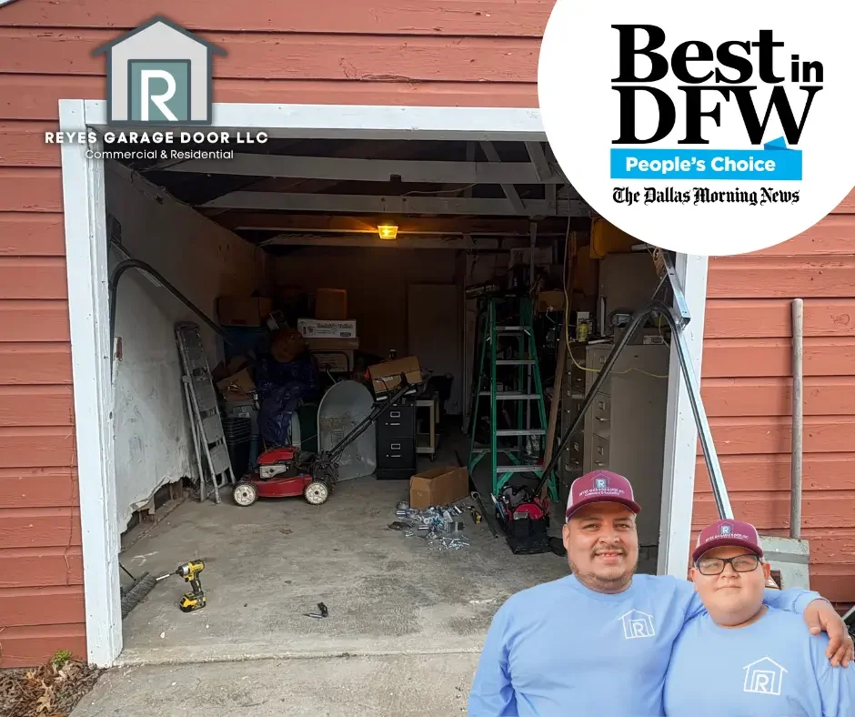 Two men wearing blue shirts and maroon caps are standing in front of an open garage filled with tools, ladders, and storage boxes, with a red wooden house behind them.